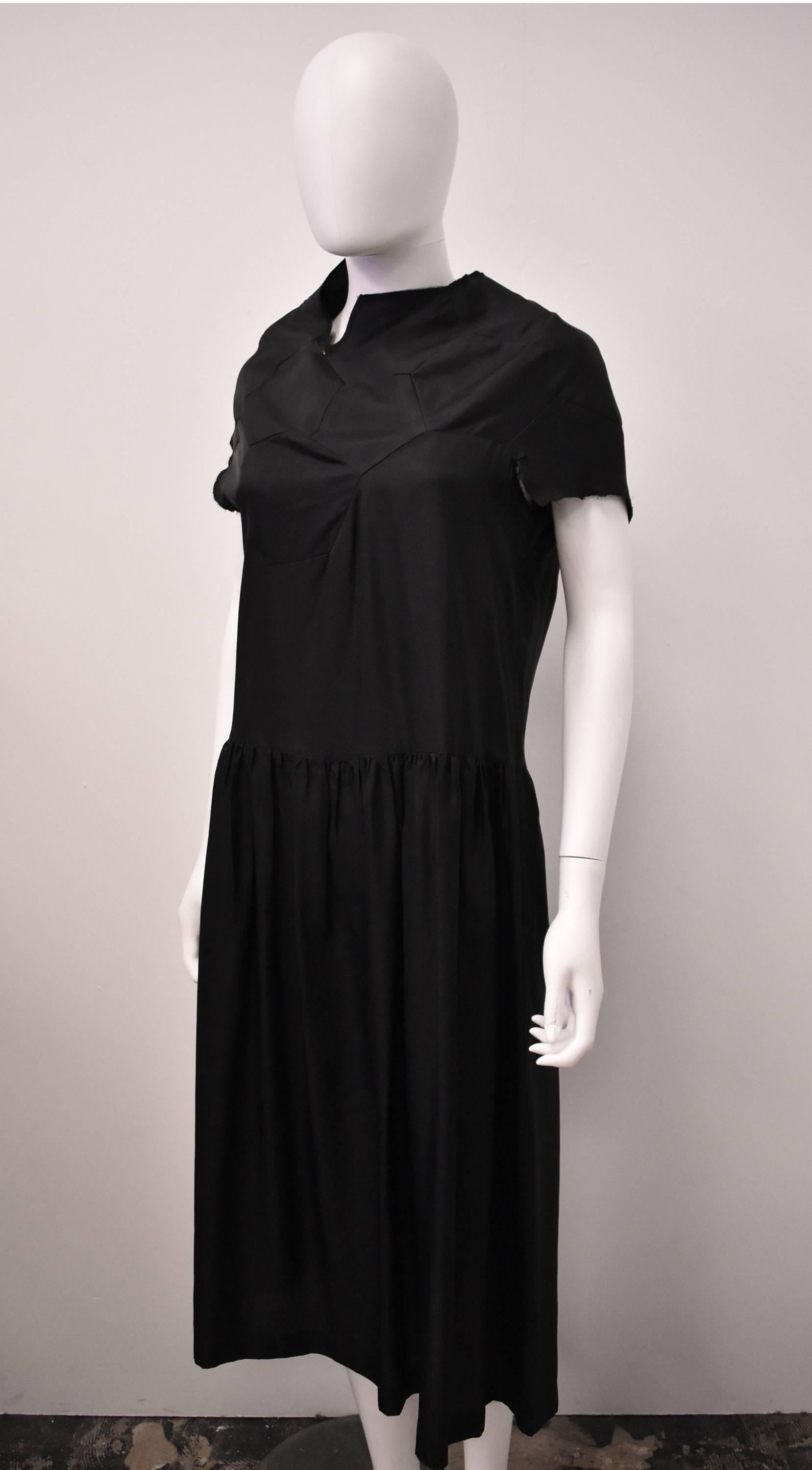 A black calf length dress from Comme des Garcons’ 2008 collection. The dress has a simple shape with a cap sleeves, straight shape, dropped waist and slight gathering at the skirt. However, as is to be expected from Comme des Garcons, there is a