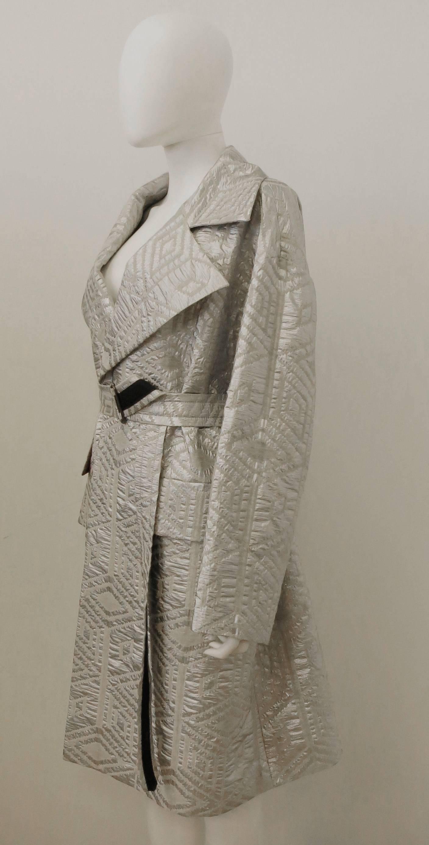 An oversize silver brocade coat from the Autumn/Winter 2014 Dries Van Noten collection. The coat has a long length with a large oversize collar, voluminous shape and attached belt. The coat is made from a wool and synthetic blend metallic brocade in