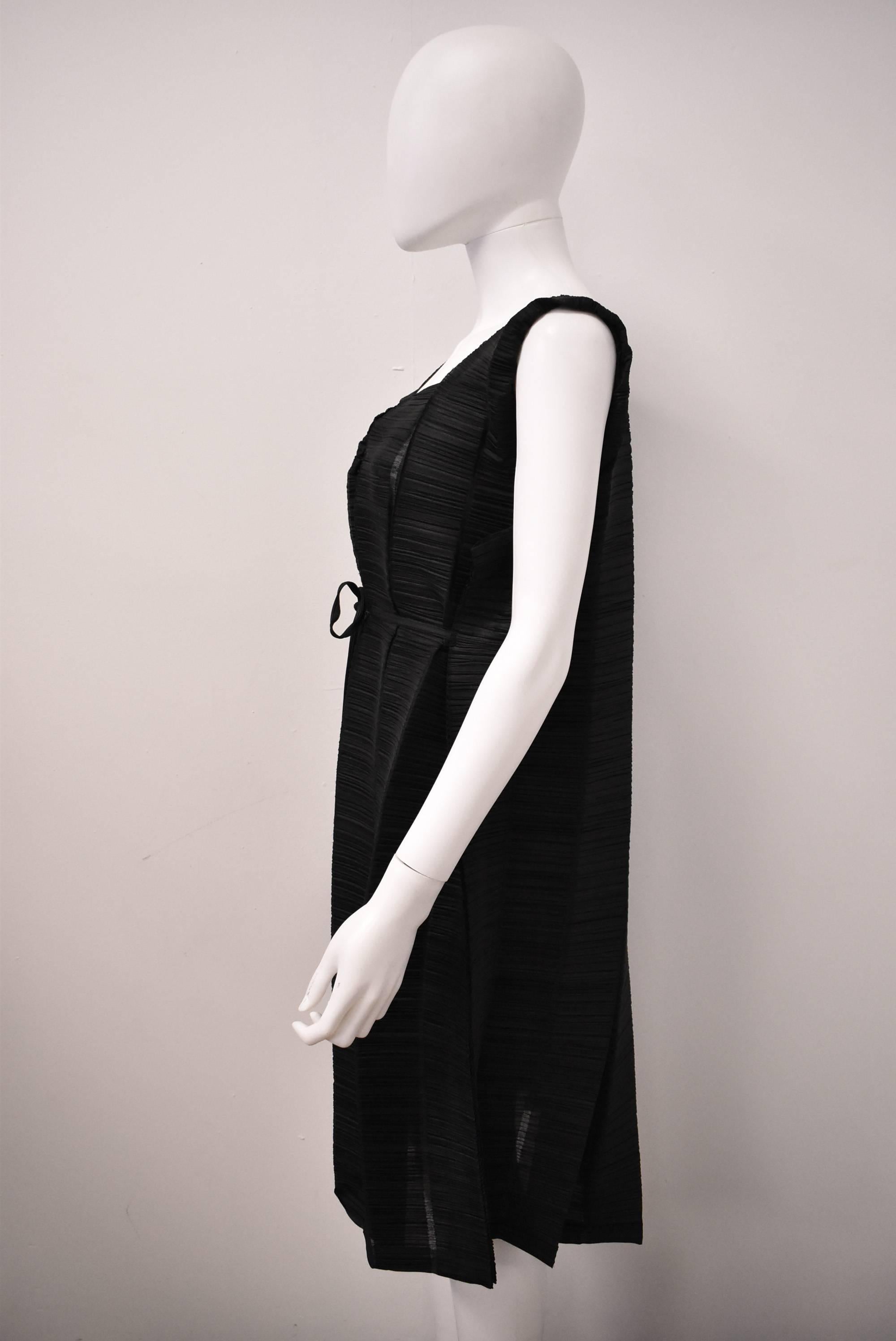 A black pleated dress/cardigan from the Issey Miyake Pleats Please Line. The piece can be worn in two ways, as a sleeveless shift dress or draped cardigan with tie fastening at the front. The piece is constructed from numerous vertical panels that