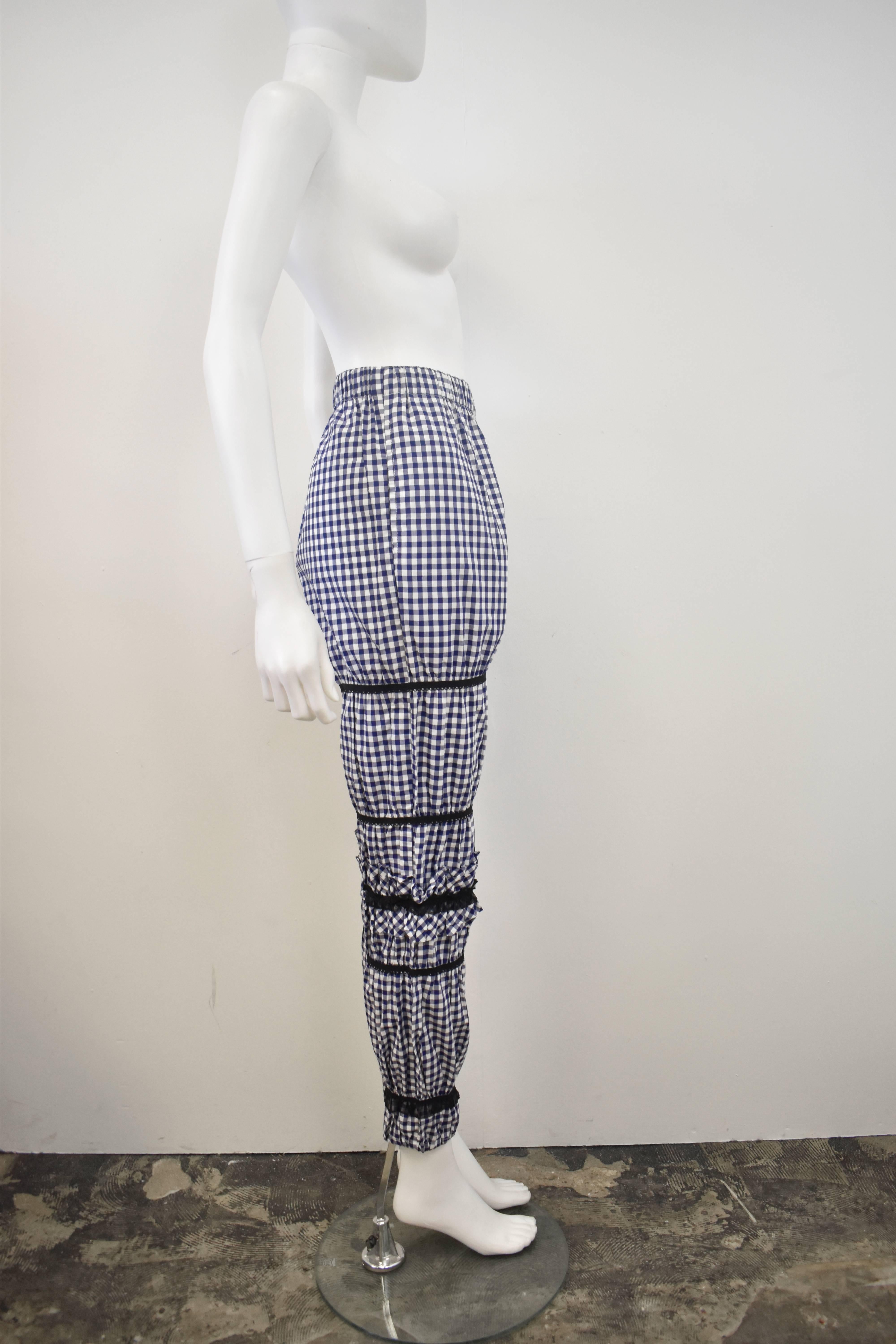 A pair of unusual and interesting trousers from Comme des Garcons. The trousers are made from a blue and white gingham cotton with contrast black bands made of ribbons and trimming that create a tapered shape. There is also an attached ruffle panel