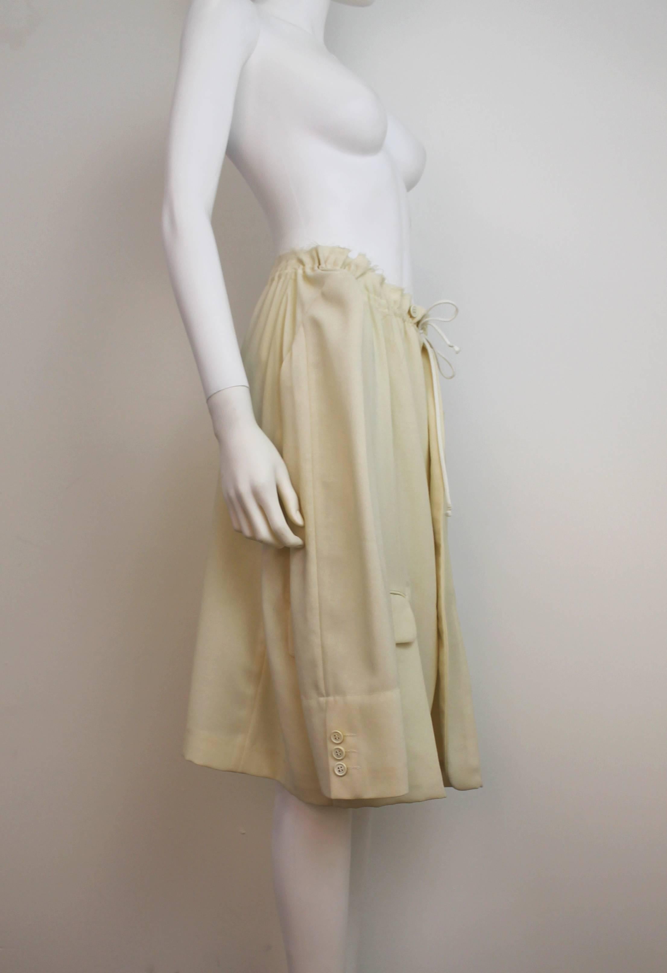 Cream Comme des Garcons jacket/skirt, which features a drawstring neck/waist and frayed edges. Can be worn as either a jacket or a skirt. From Spring/Summer 2001.
