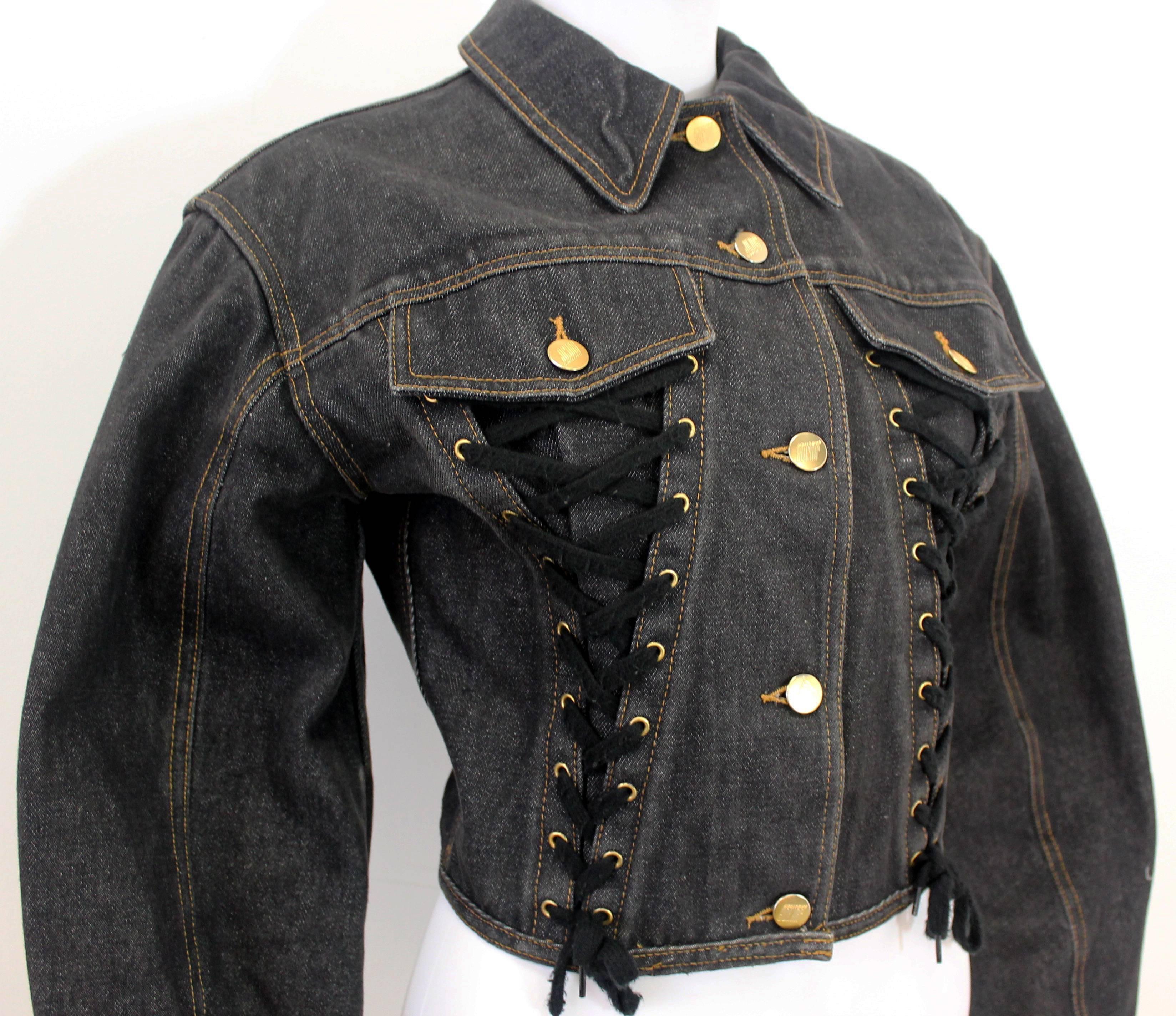 Dark denim Junior Gaultier jacket with adjustable lace-up front, reminiscent of a traditional corset. Features a puffed sleeve and gold buttons.
