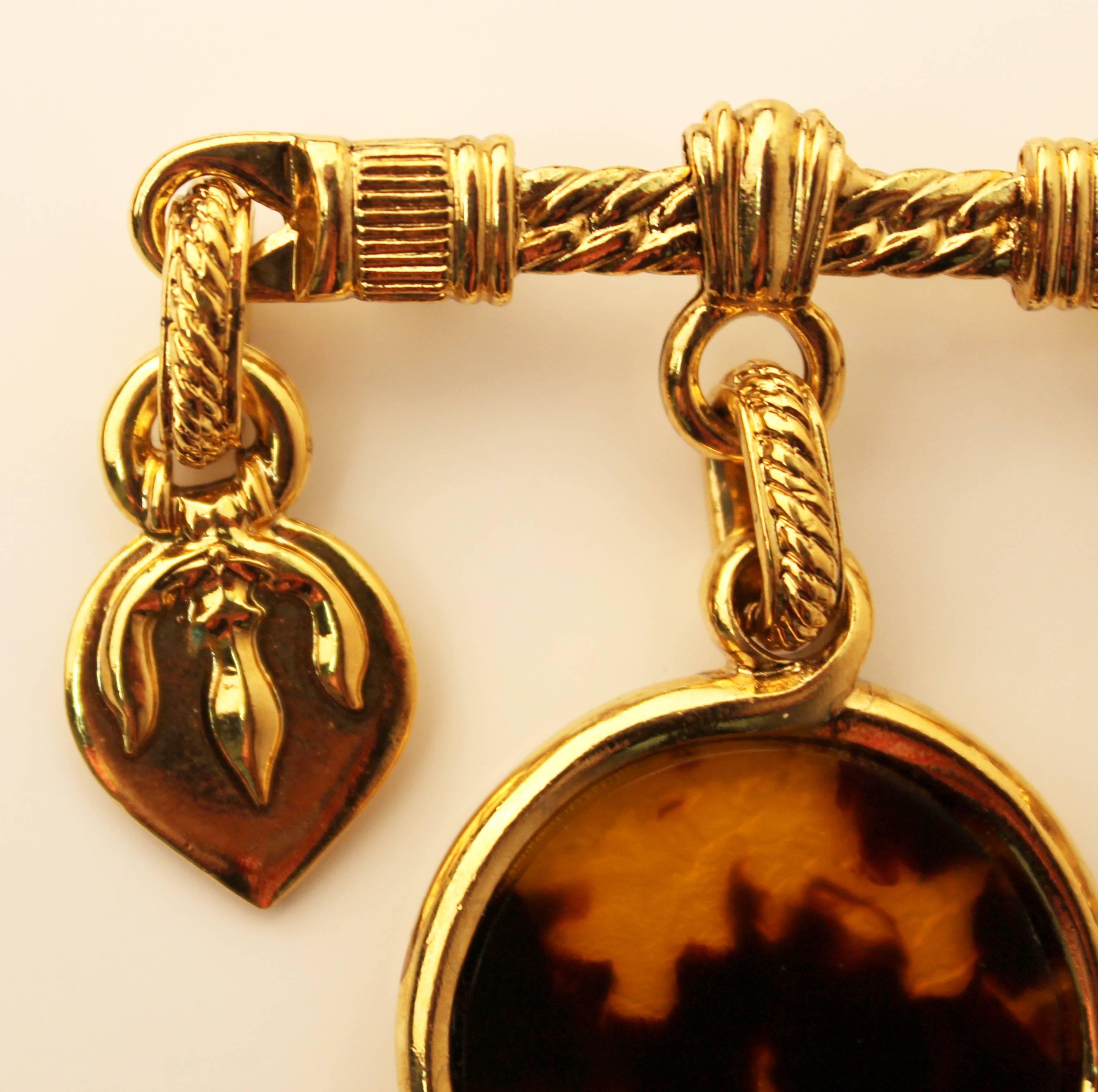 Very rare and unique vintage gold-plated brooch from Yves Saint Laurent. Features two small hanging charms on either side (one featuring a trident) and a larger tortoise shell charm in the middle. Estimated to be from before 1990.