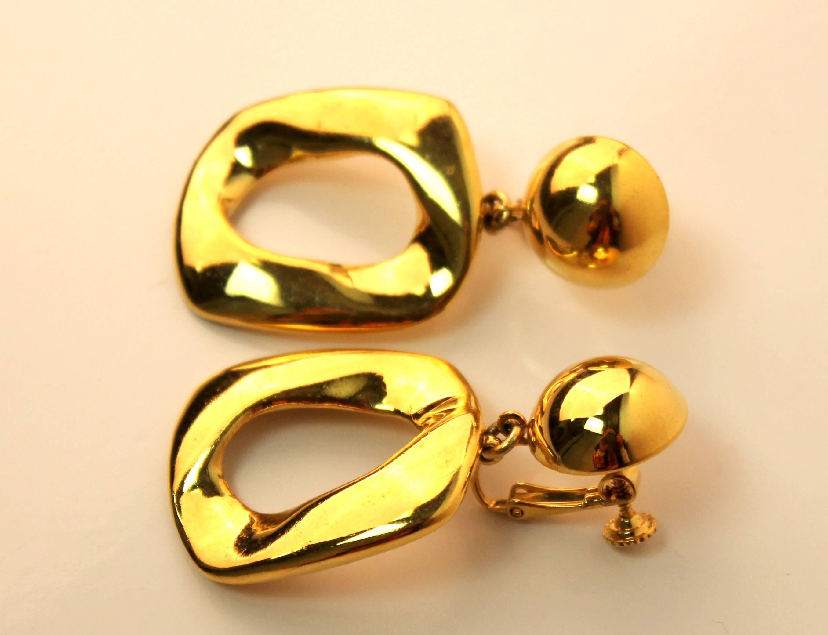 Classic vintage gold-plated earrings from Yves Saint Laurent. Features a round distorted square shape hanging from a convex circle. Has a twist clip closure.