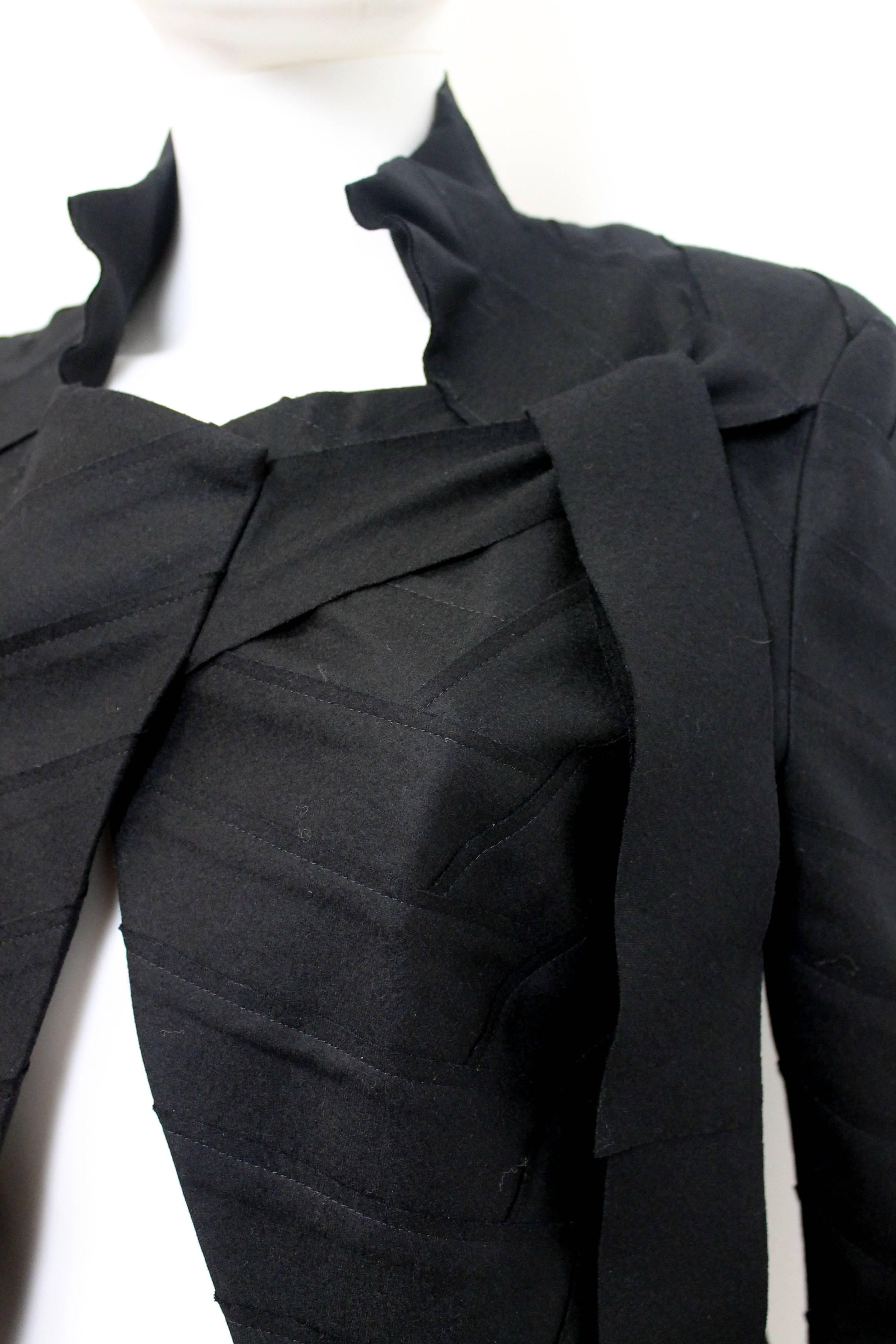 Issey Miyake black chevron panel fitted jacket with asymmetric tie neckline. We believe to be early 2000s in date.

This Issey Miyake black cropped-jacket is made entirely out of chevron shaped interlocking wool patchwork. The jacket is
