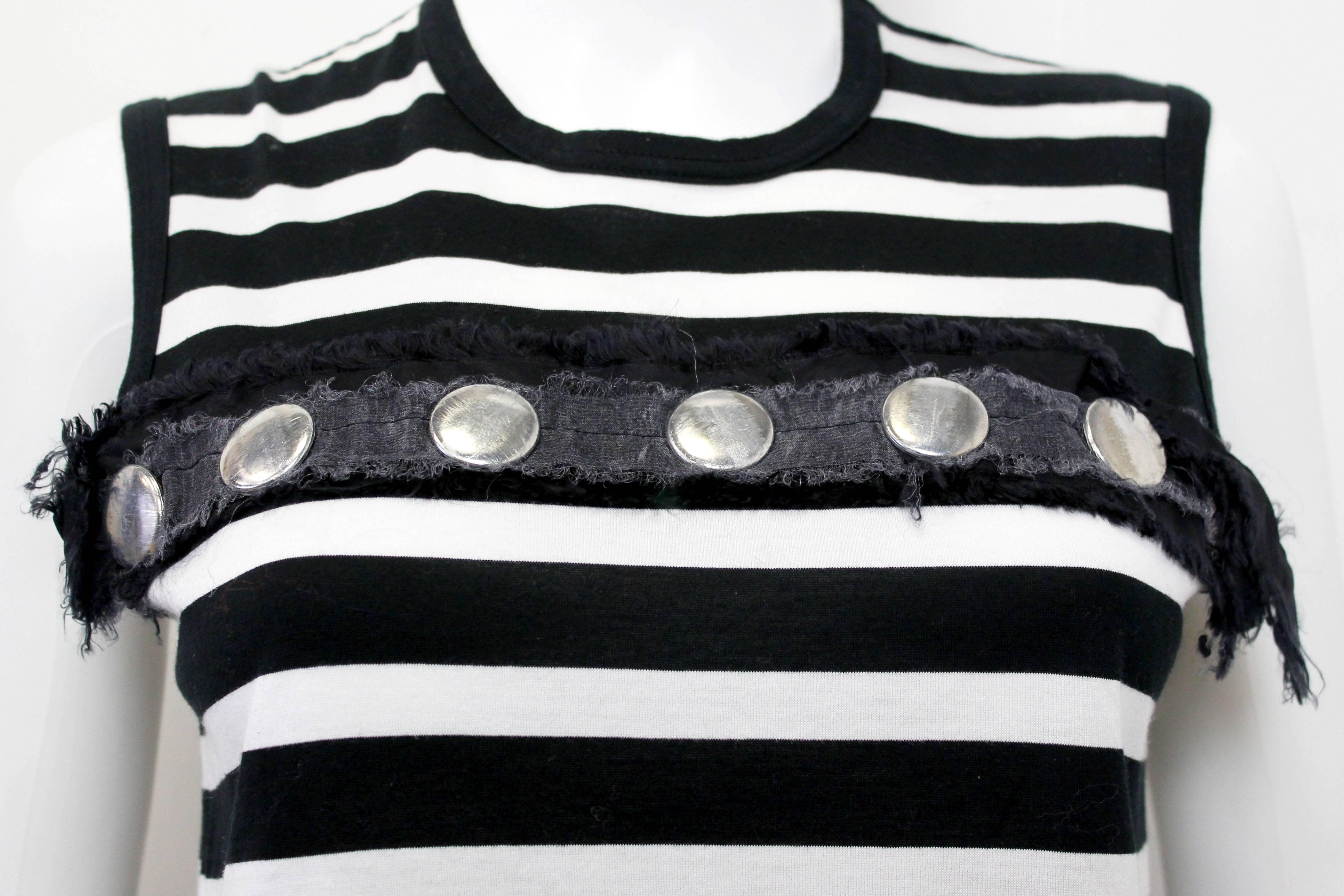 This Comme Des Garcons vest is from the Tricot line. The vest is made from a horizontal striped jersey cotton.
The vest is also embellished with a raw edged fabric and then studded with silver circular distressed button like studs.
