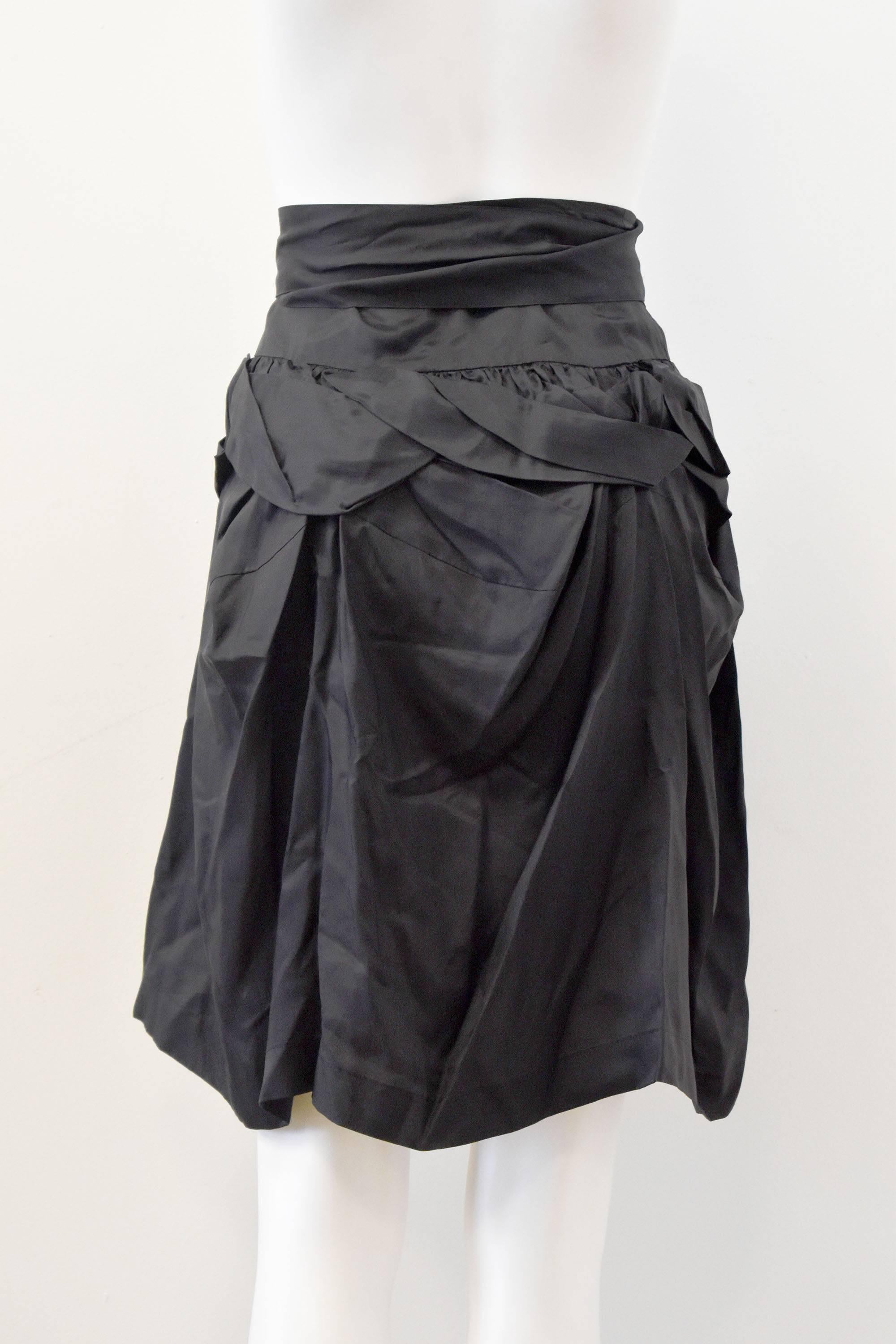 A cute black ruffled skirt from Comme des Garcons’ diffusion line ‘Tao’. The skirt has a panel that folds over with ties to form a bow and a ‘uneven’ stitched section that forms the top ruffle. The skirt is made of a silky material and falls to