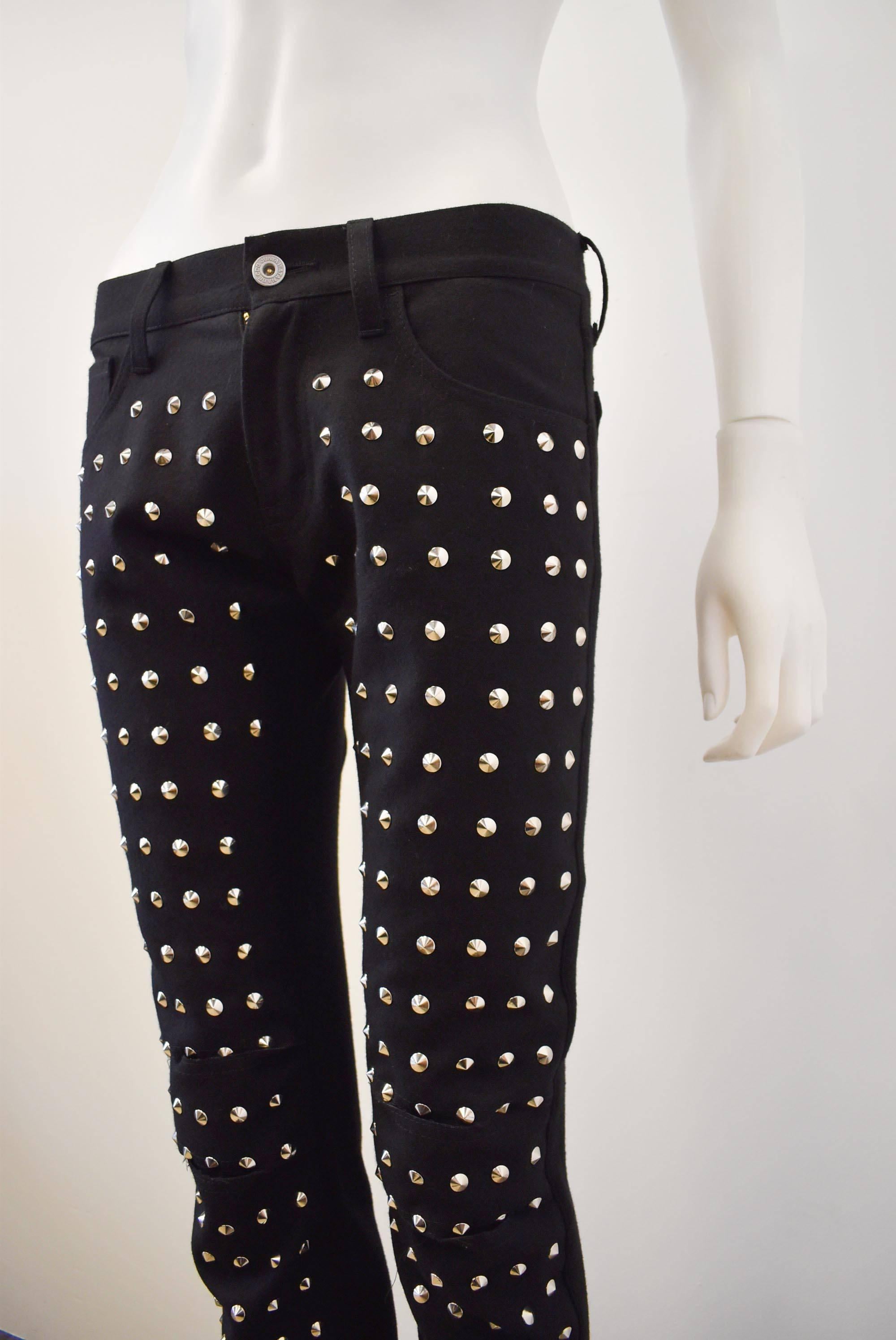A pair of black jeans-like cotton stretch trousers by Junya Watanabe. The 
front of the black jeans are decorated with rows of metal studs and incisions 
in the knees for an interpretation of the ripped denim style, creating a modern punk