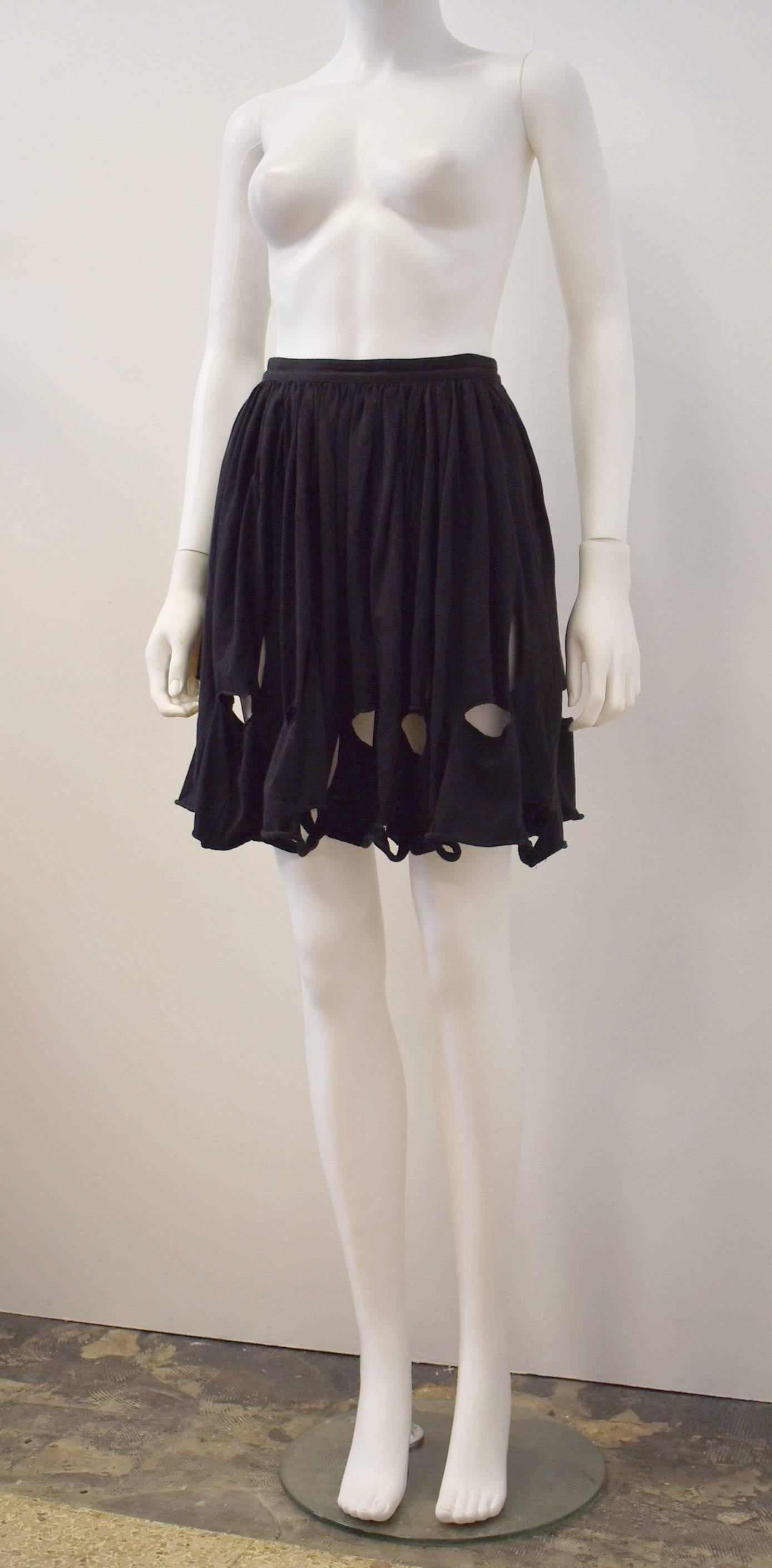 Comme des Garcons short black pleated/flared skirt with cut-out details along the hem. The holes are cut in an elliptical shape, both horizontally and vertically to create a ‘deconstructed’ aesthetic that is synonymous with the brand. The skirt is