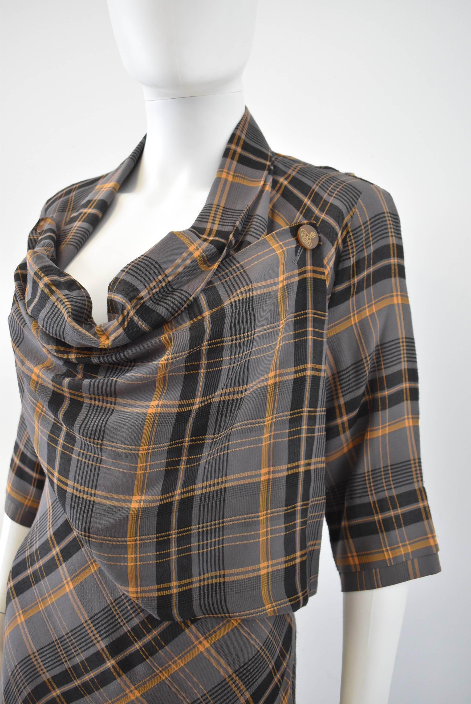 A grey tartan check dress from Vivienne Westwood’s diffusion line Red Label. The dress has a simple shape that skims the waist and flares out at the skirt. The dress has a cowl neckline that is created by two bib panels that crossover and button at