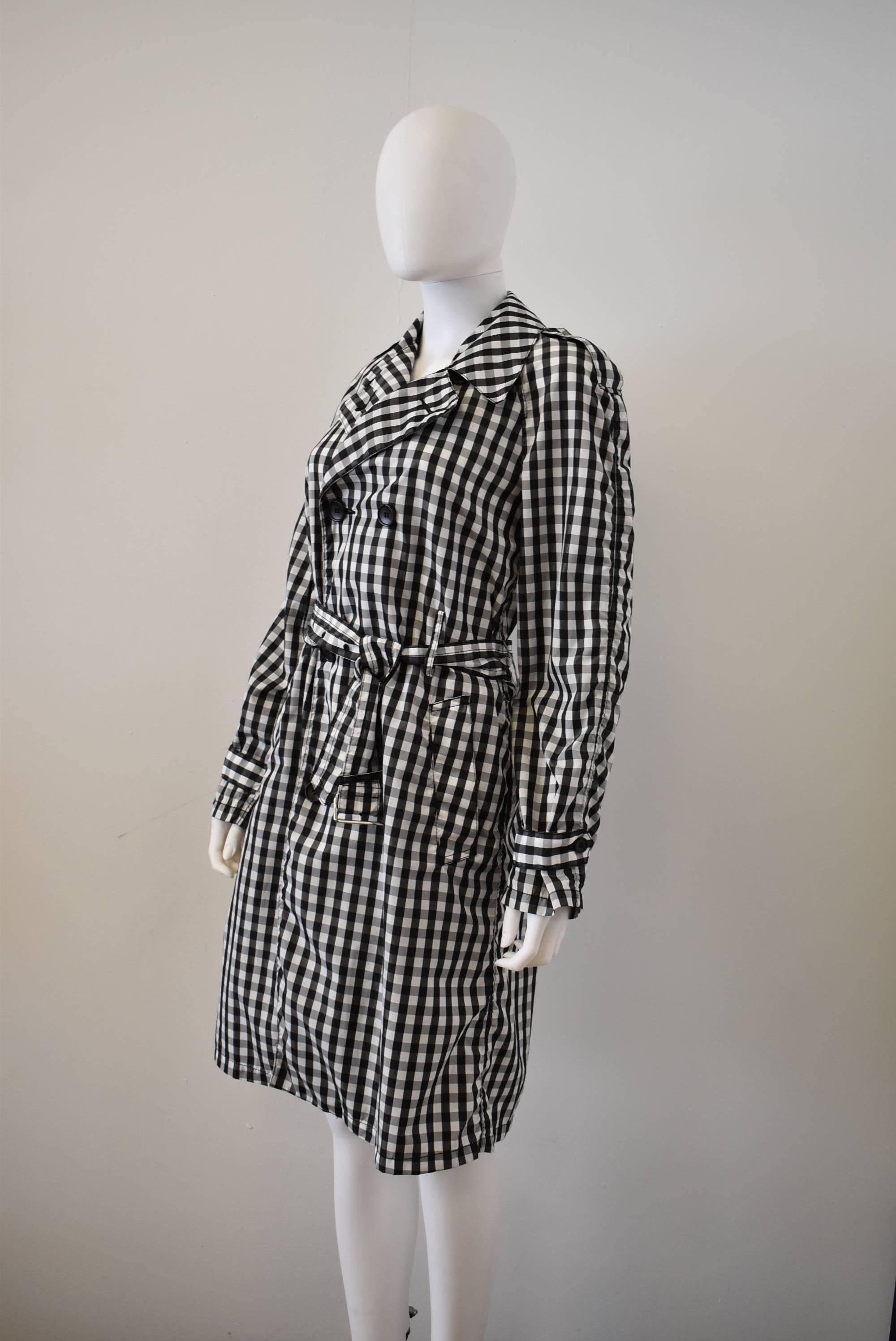 An classic black and white trench check trench coat from Comme des Garcons, with double breasted button fastening, notched collar, pockets and an attached belt around the waist. Year unknown.