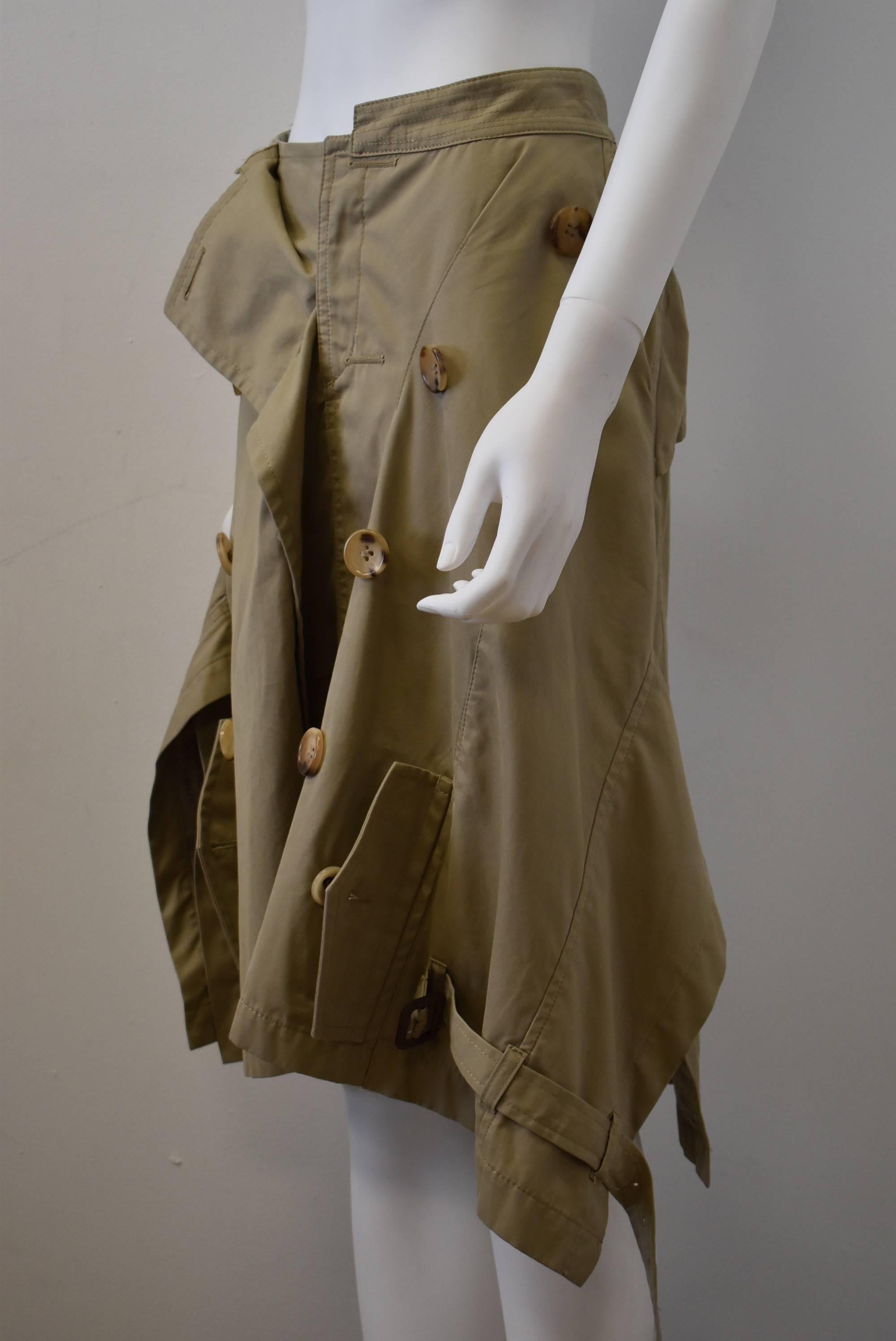 A deconstructed trench coat dress from Comme des Garçons designer Junya Watanabe. The waistline of the skirt is made from the coat collar and the double breasted buttons run along the length of the skirt. There are pockets at the bottom of the