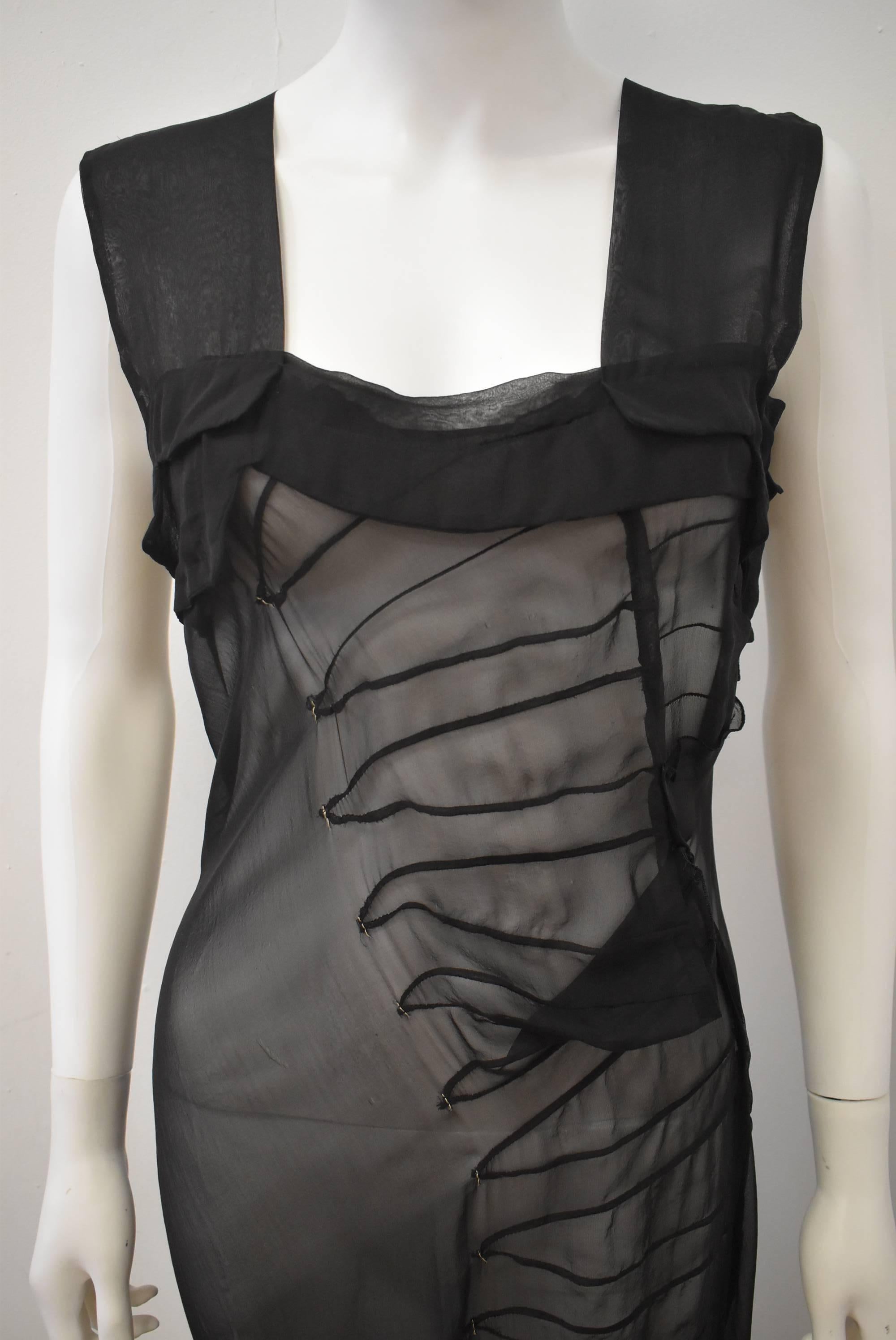 A black sheer maxi dress by Jil Sander. The dress features a repetition of seams that resemble articulated armour panels. The inserts are finished with tiny hand sewn silver stitches at each point. The dress also features a train at the back and a