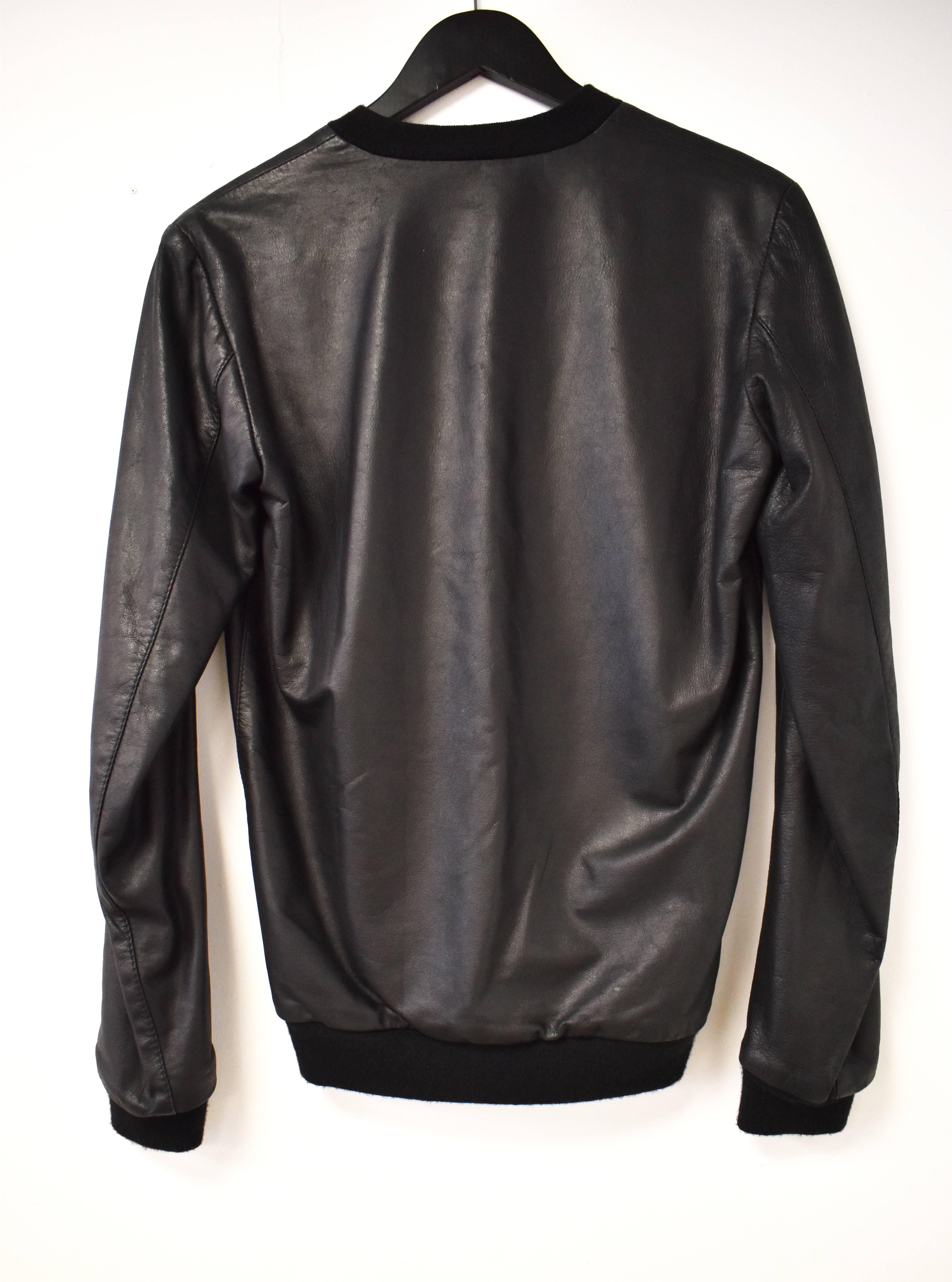 A leather Raf Simons sweater-style leather top. The top has a stitched and applique diamond design on the front with threaded leather straps mimicking the design of a knitted sweater. The top is long sleeved and made of 100% leather with a silk