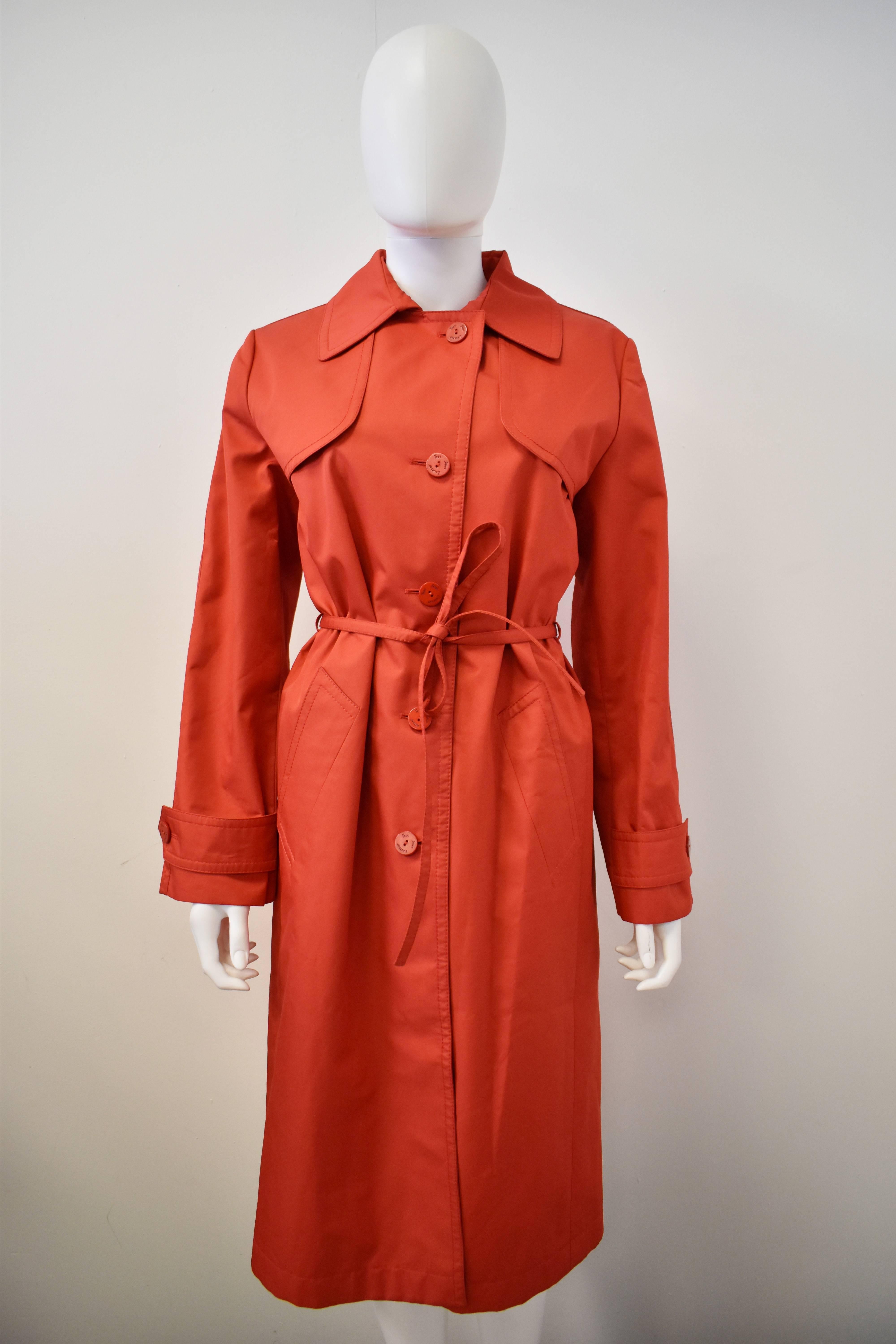 A beautiful 1980’s vintage red trench coat from the Yves Saint Laurent subsidiary line Rive Gauche. The coat has a classic single breasted trench design with gun flaps on either side of the bust, deep back yoke, vent at the back and a thin tie at
