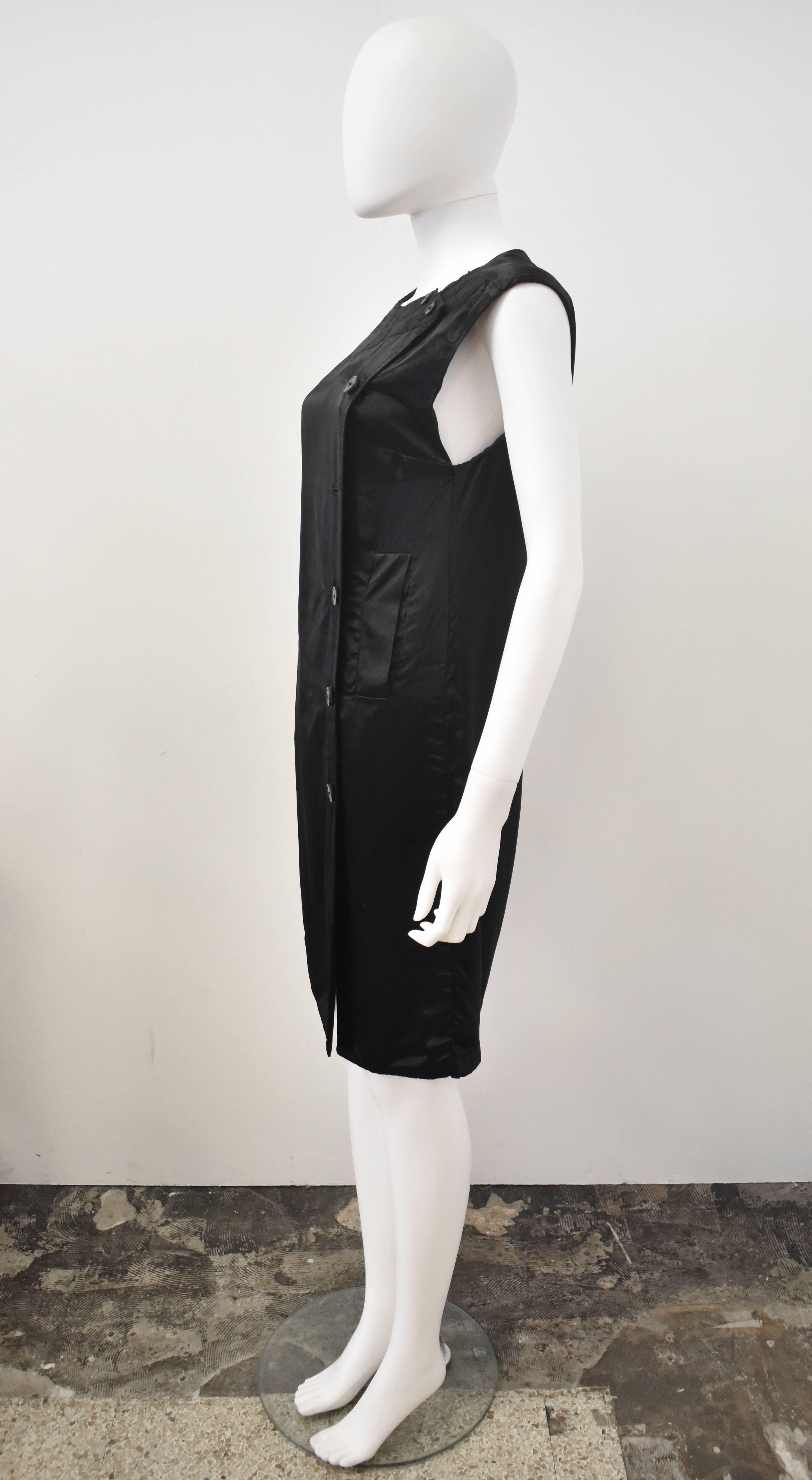 A black dress with button closure to the side, two side slant pockets, and a round textured collar by Dries Van Noten. Made of a light, shiny viscose-like fabric. This a sample piece; it does not feature a care label. A button is missing but it does