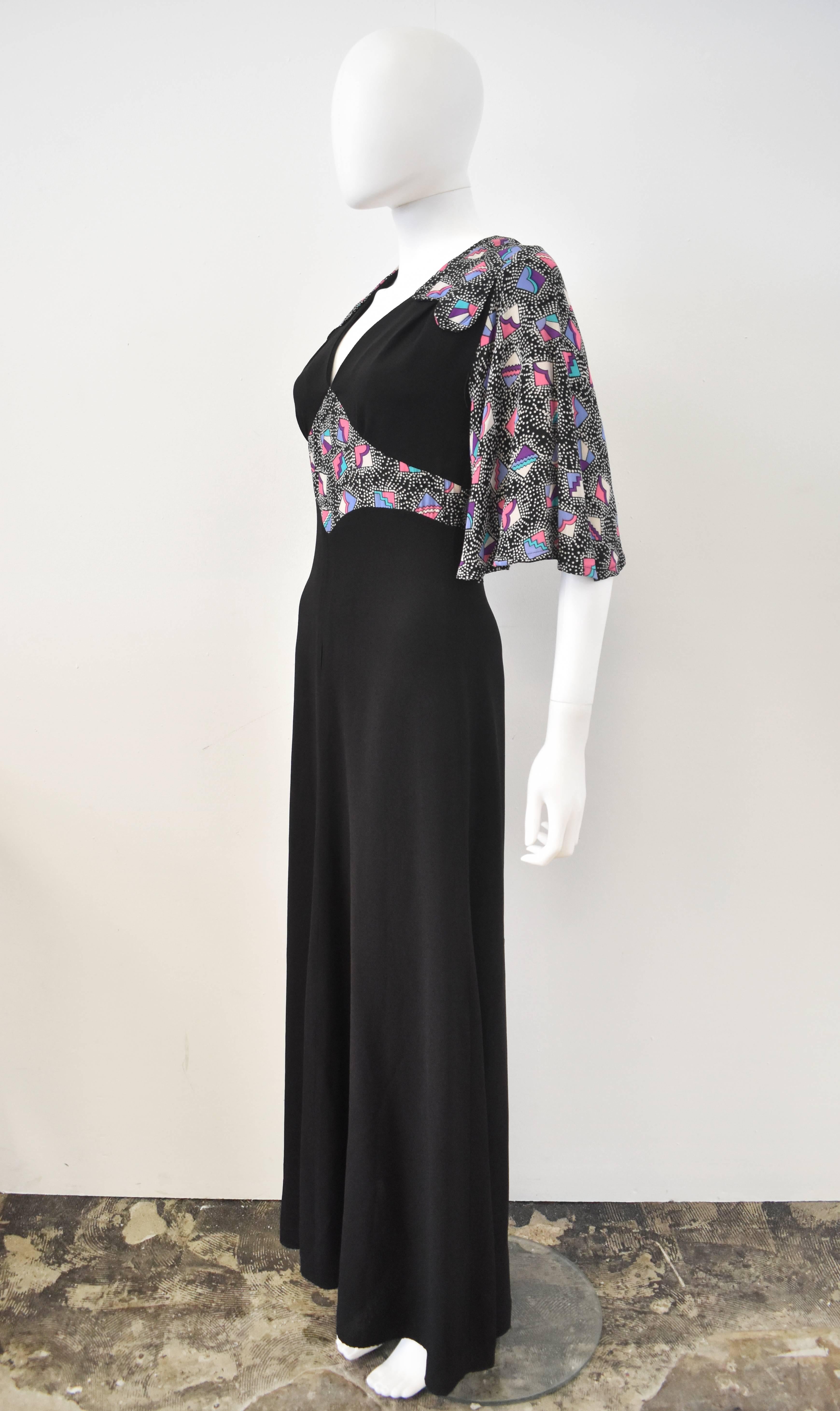 From the iconic London boutique Bus Stop which opened in 1968. A long black crepe dress with flared mid-length sleeves and abstract motifs along the waist and shoulders. The cut is reminiscent of the 1970s, while the colorful abstract motifs hint to