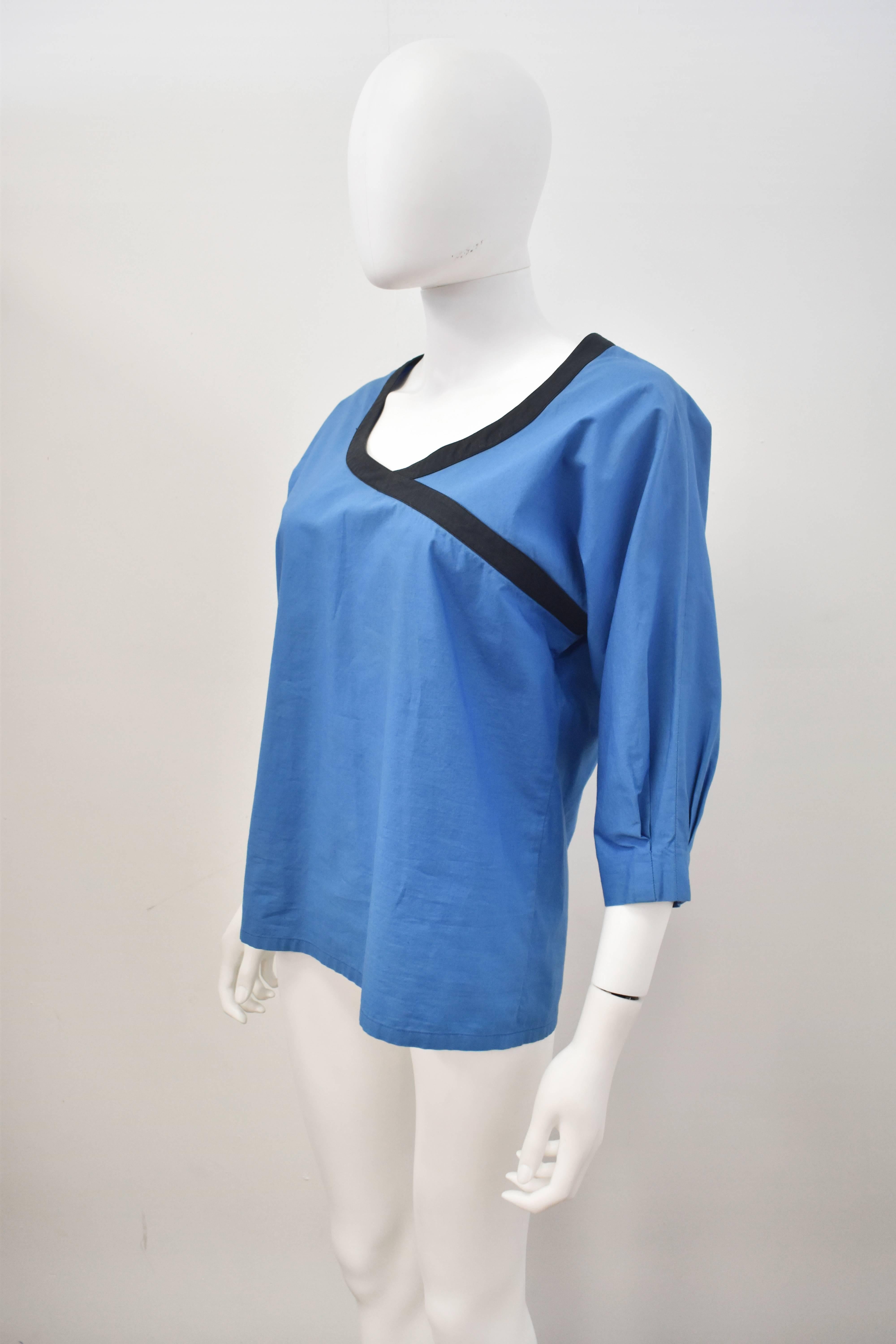 A blue raglan three-quarter length sleeve boxy top by Lanvin. It features a black band along the neckline that extends diagonally towards the left sleeve. The sleeves are pleated at the cuff to create a light balloon-like effect. Apart from very
