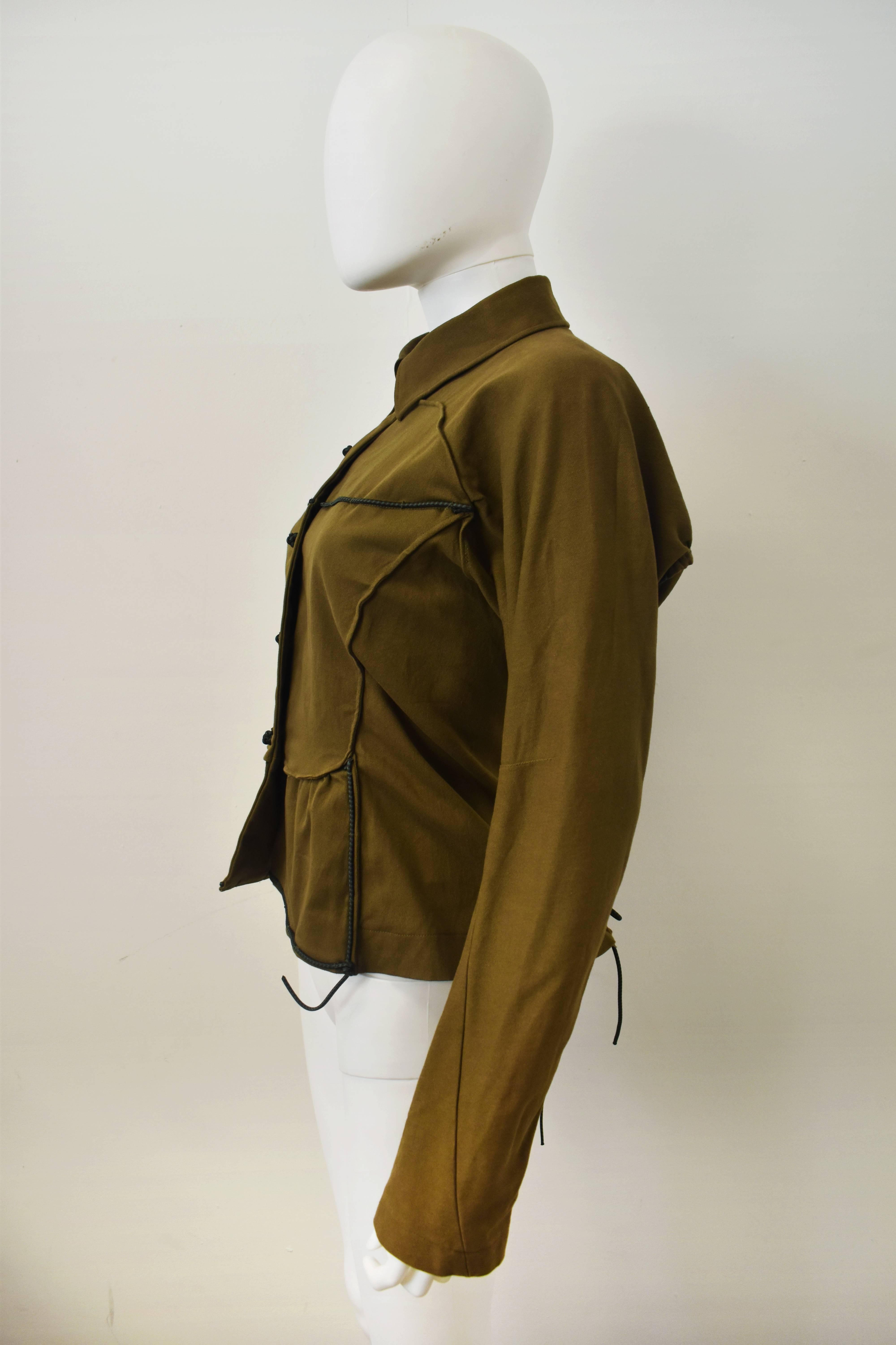 A khaki jacket with innovative elastic piping and an elastic corset tie-back details from Issey Miyake. Giving the classic safari jacket a sporty twist, the jacket has an unusual bib front with contrast elastic piping and elastic knot buttons. As