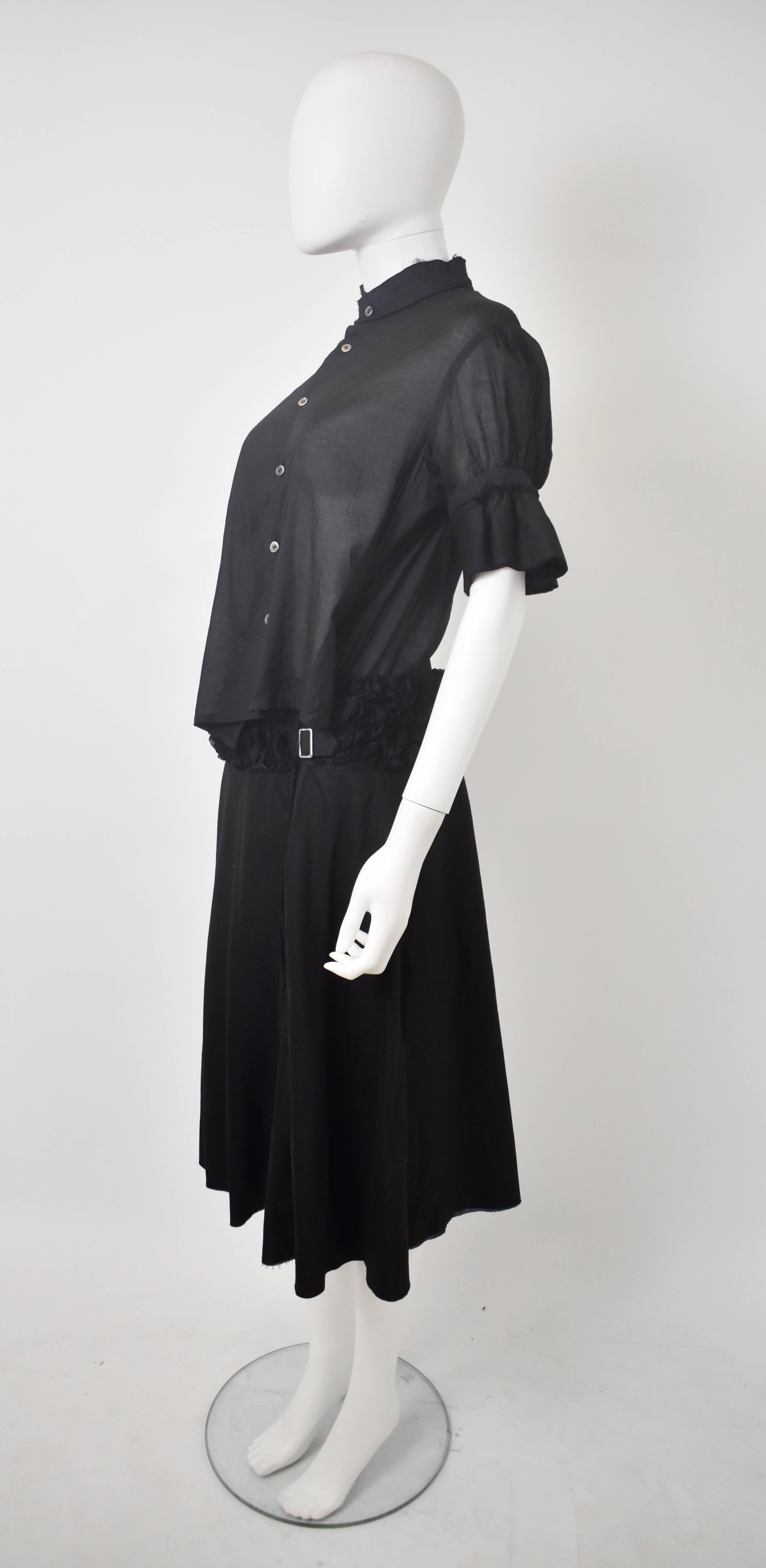 A 2007 Comme des Garcons Tricot black one-piece dress constructed from a short-sleeve shirt and Kilt skirt. The shirt section of the dress is made from a semi-sheer cotton with mandarin collar, button-up front and asymmetric dart details that create