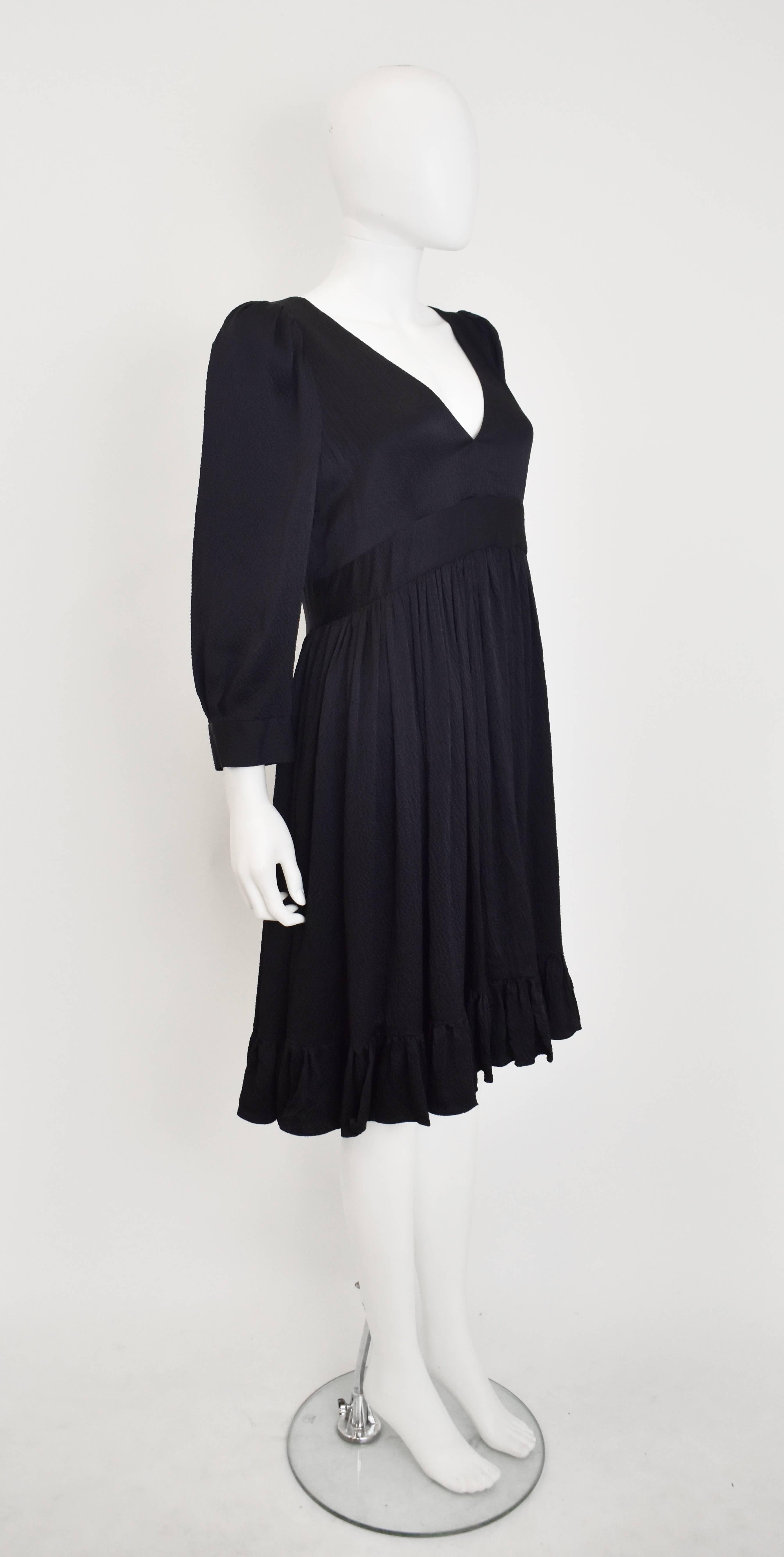 An elegant dress from Balenciaga’s Silk collection. The dress has a classic shape with a V-neck, fitted waist, bell sleeves with a cuff and a ruffled hem. The dress is made from a textured black silk and falls to just above the knee. It is an