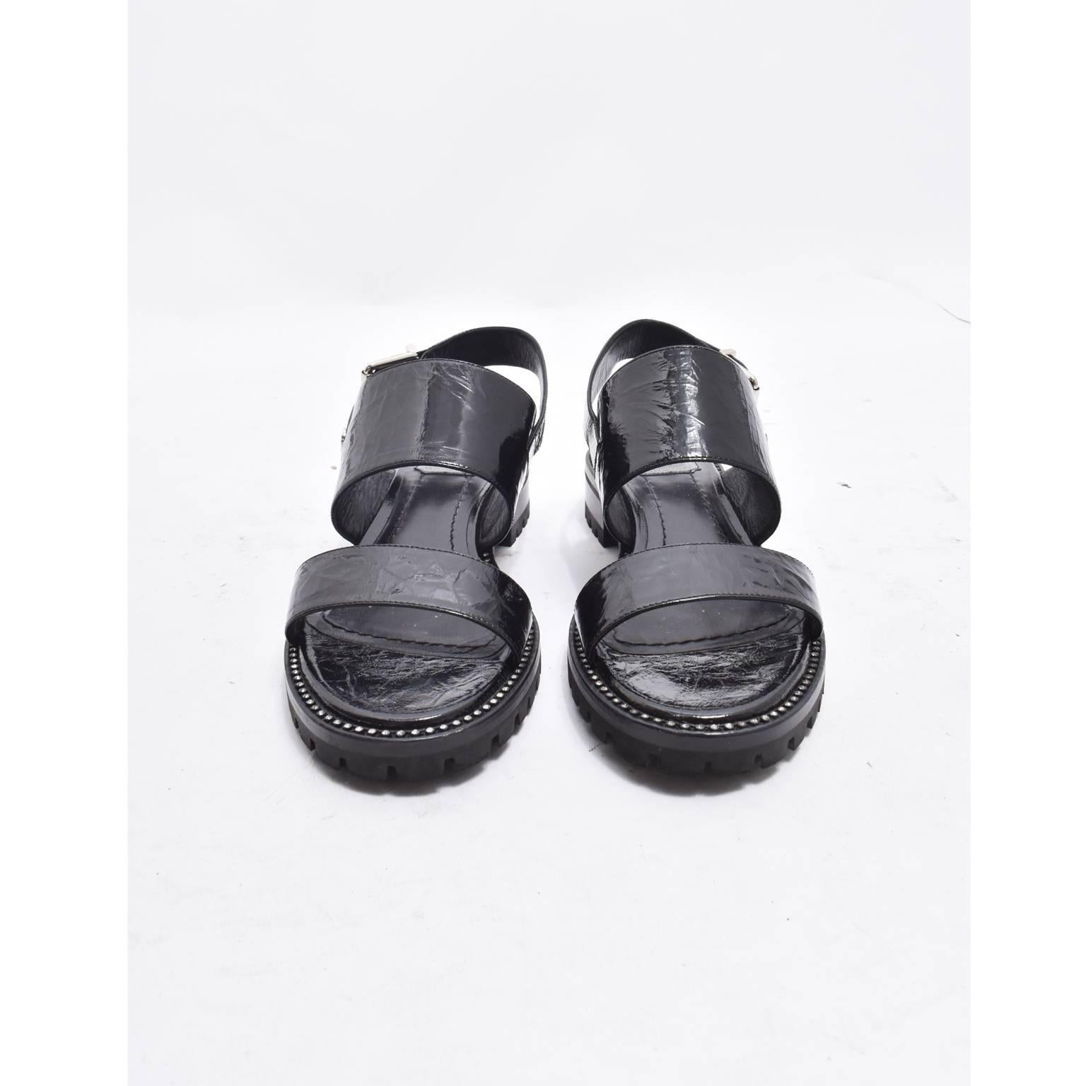 A pair of black leather sandals by Christian Dior. The sandals have two straps and a buckled strap at the back for fastening and a thick rubber sole with treads. They feature silver hardware details and crystal embellishments around the sole of the