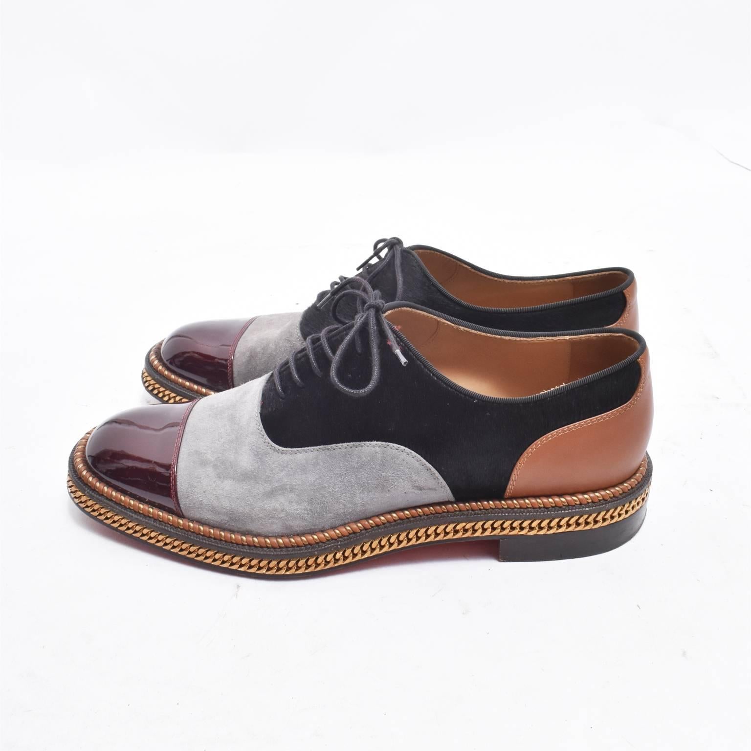 A beautiful pair of Christian Louboutin Oxford Shoes. The shoes are made from mixed, multicoloured leather panels including red patent leather, grey suede and black and brown leather. There is a gold metal chain that frames the shoe around the sole,