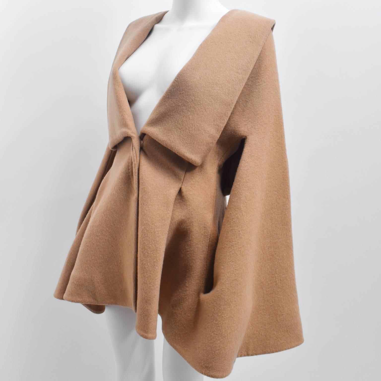 A beautiful Alexander McQueen camel coat made from soft cashmere. The coat has an unique shape; with a large oversize collar, fitted waist, and softly pleated bottom. The coat features exaggerated bell sleeves that are connected to the main body of