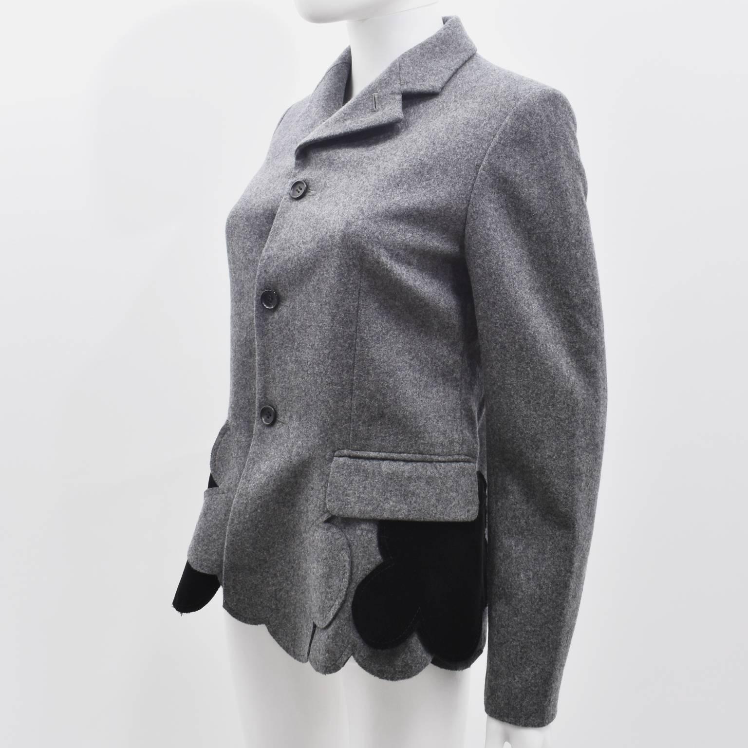 A grey wool blazer with velvet panel inserts from Comme des Garcons. The blazer has a straight cut with a notched collar, button down front and two pockets at the hip. In a Comme twist on a classic jacket, it has an irregular scalloped hem and