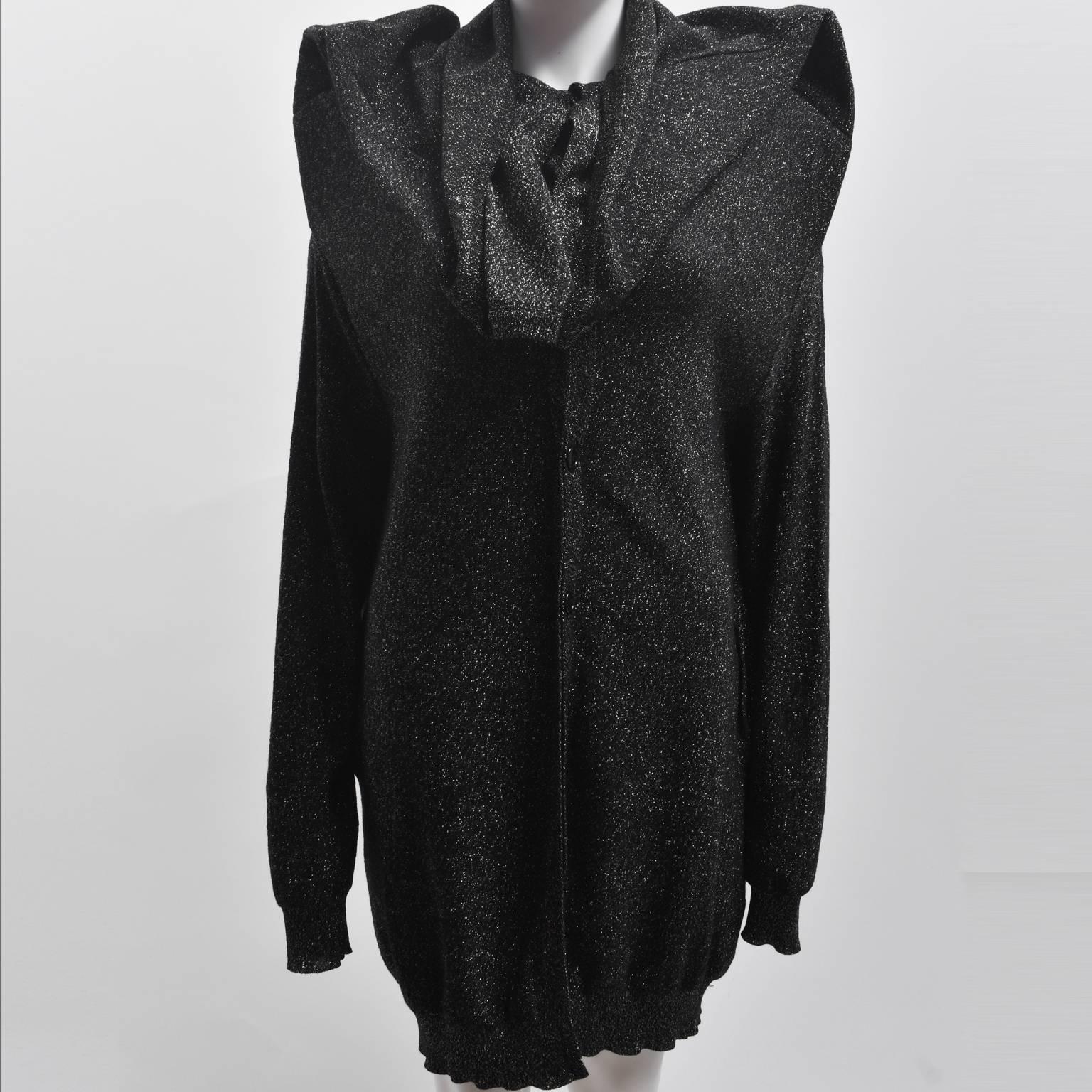 A theatrical and avant-garde black and silver glitter knit from Maison Martin Margiela. The longline jumper has a button down front and long sleeves and features structured inserts in the shoulders that create an exaggerated shoulder silhouette.