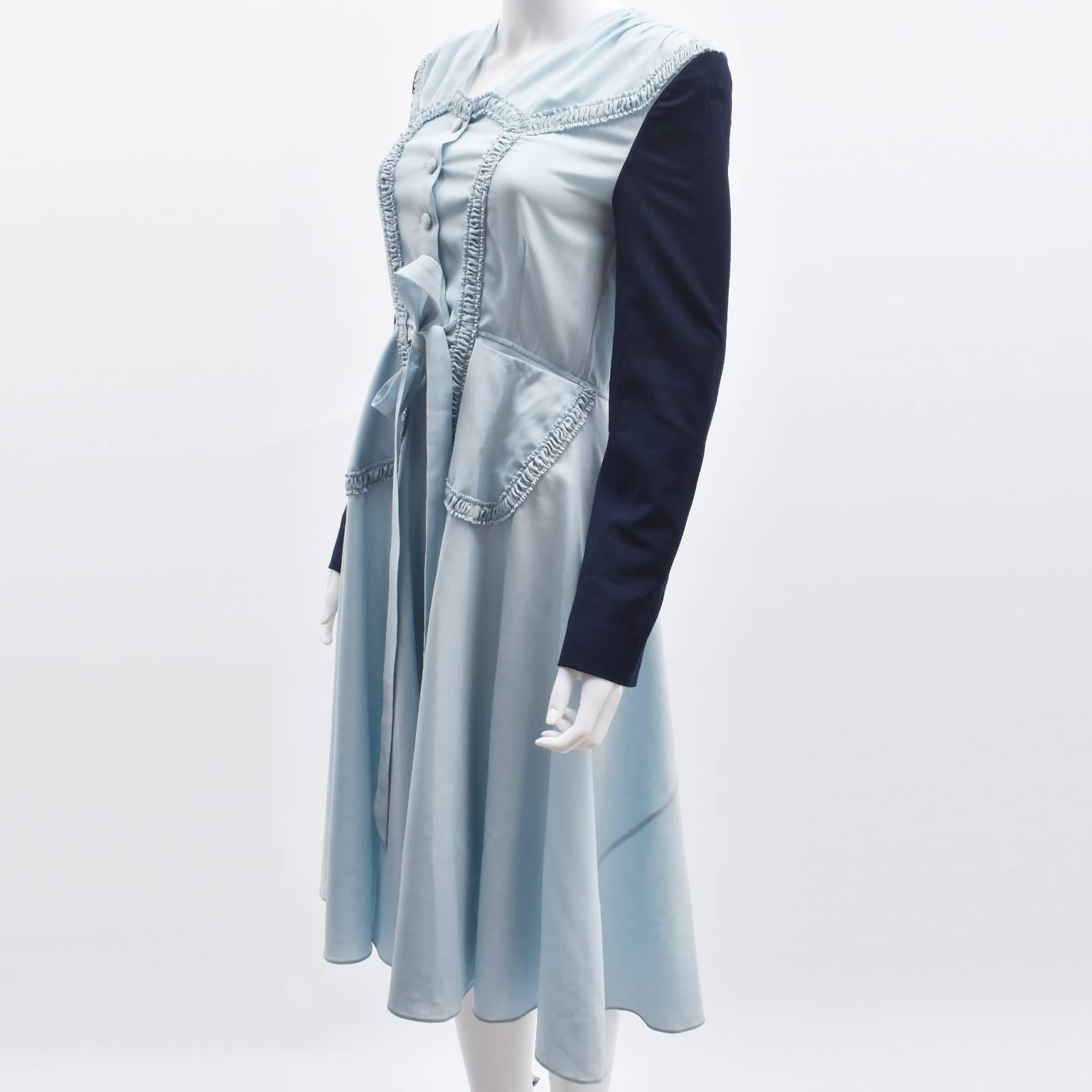 A light blue Maison Margiela dress with a vintage 1940’s silhouette. It has a fitted waist, tie-belt, shoulder pads, and ruching details on the front. Like most Margiela pieces, the dress has some unusual features, such as contrast navy blue jacket