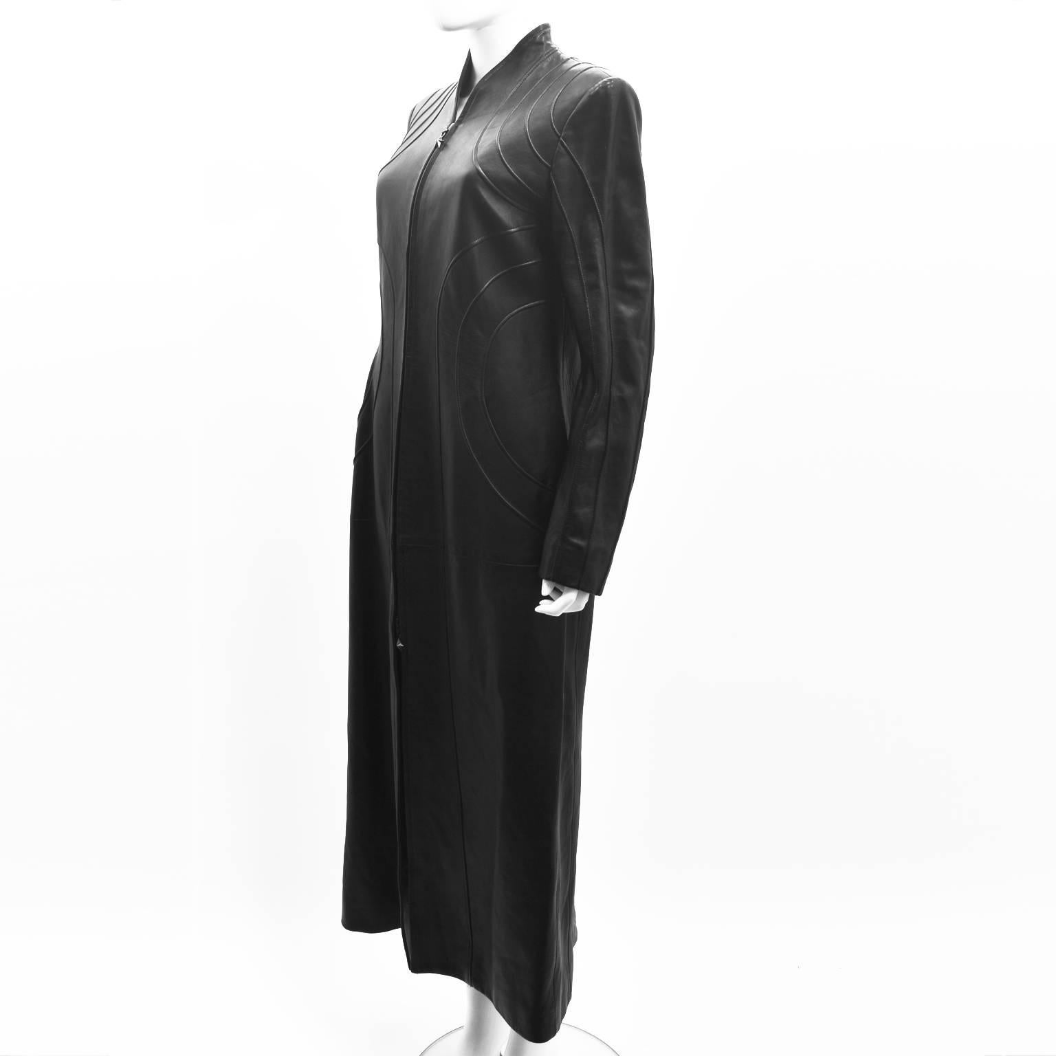 A stunning and rare black leather long coat by Thierry Mugler from the 1990’s. The coat has a long length and a slim, fitted shape with zip fastening and no collar. It also features decorative geometric seam details across the front and back of the
