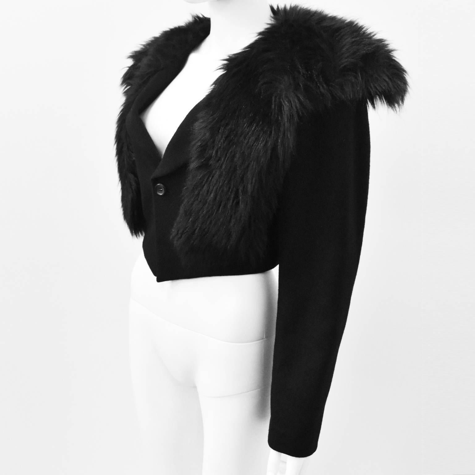 An elegant black cropped jacket with faux fur collar from Comme des Garcons. The jacket has long sleeves, v-neck, button fastening, cropped length that falls to the waist and pointed ends. It has an attached faux fur collar/shawl that covers the