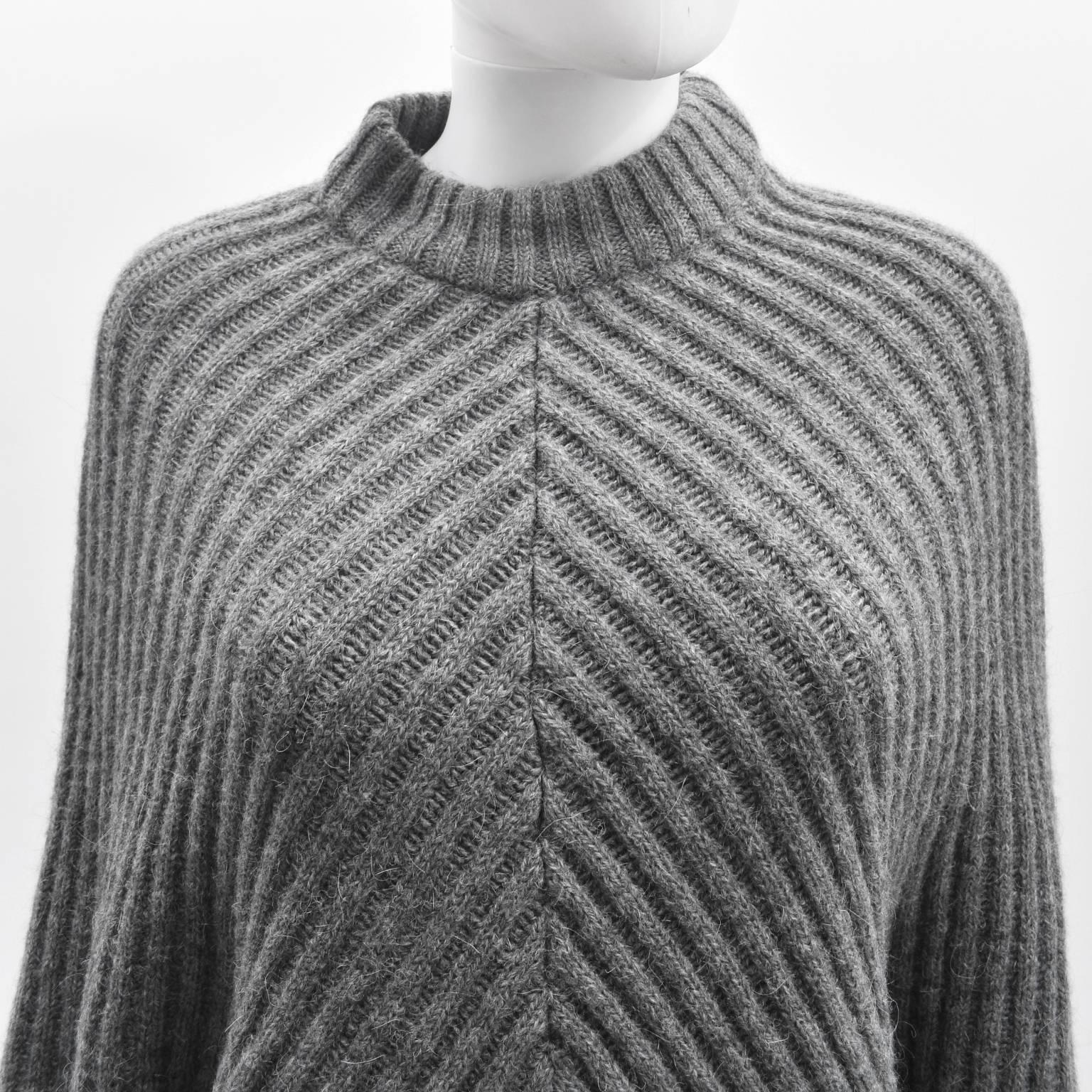 A beautiful and warm grey knit poncho by Maison Margiela's MM6 subsidiary line. 
The poncho has a simple triangular shape that covers the shoulders and arms that falls across the front and back of the body. It also has a round neckline. 
The poncho