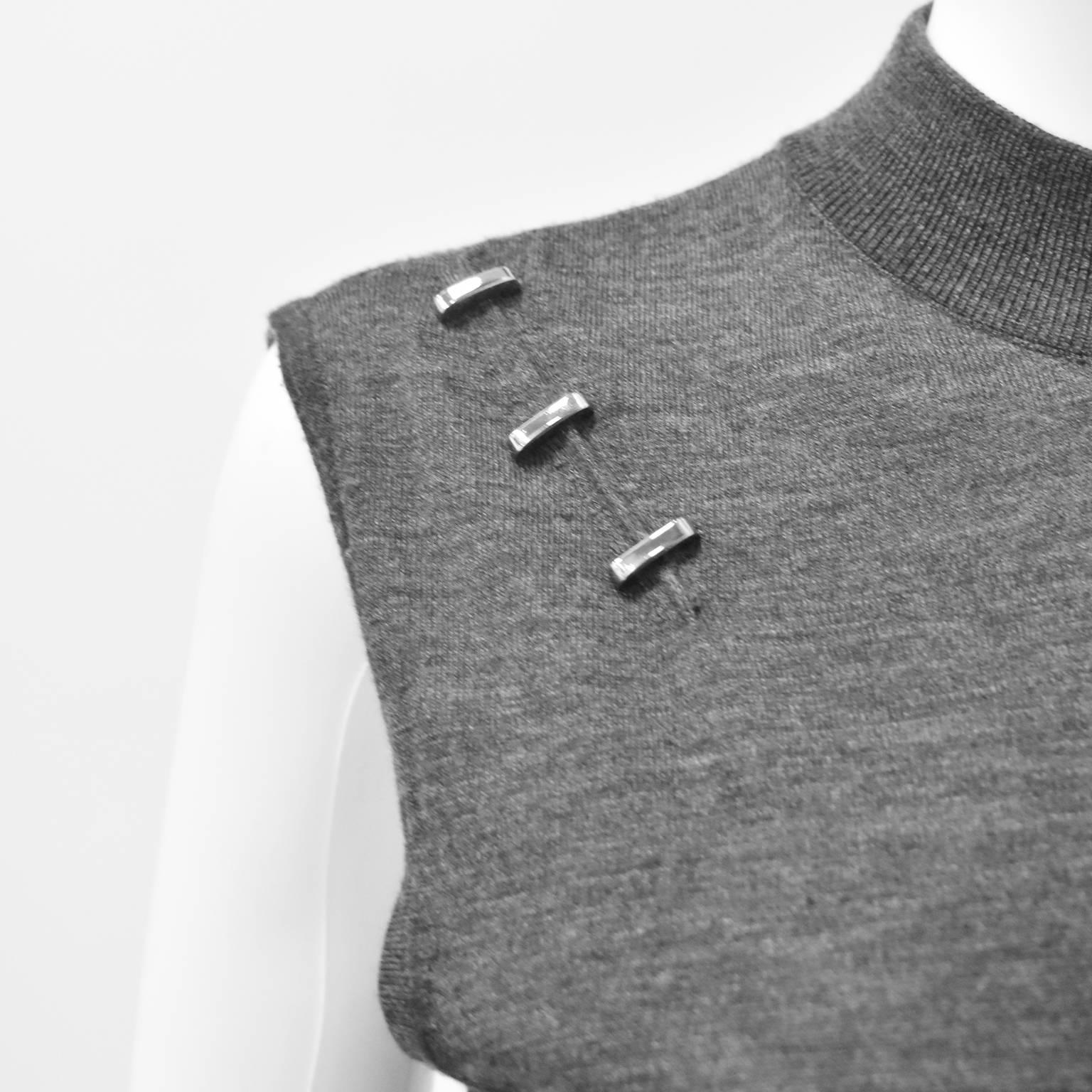 A grey knit vest top from Paco Rabanne. The top is a simple sleeveless design with wide arm holes and a high neck with a ribbed finish along the opening. The top also features silver hardware details creating a line from the shoulder down towards