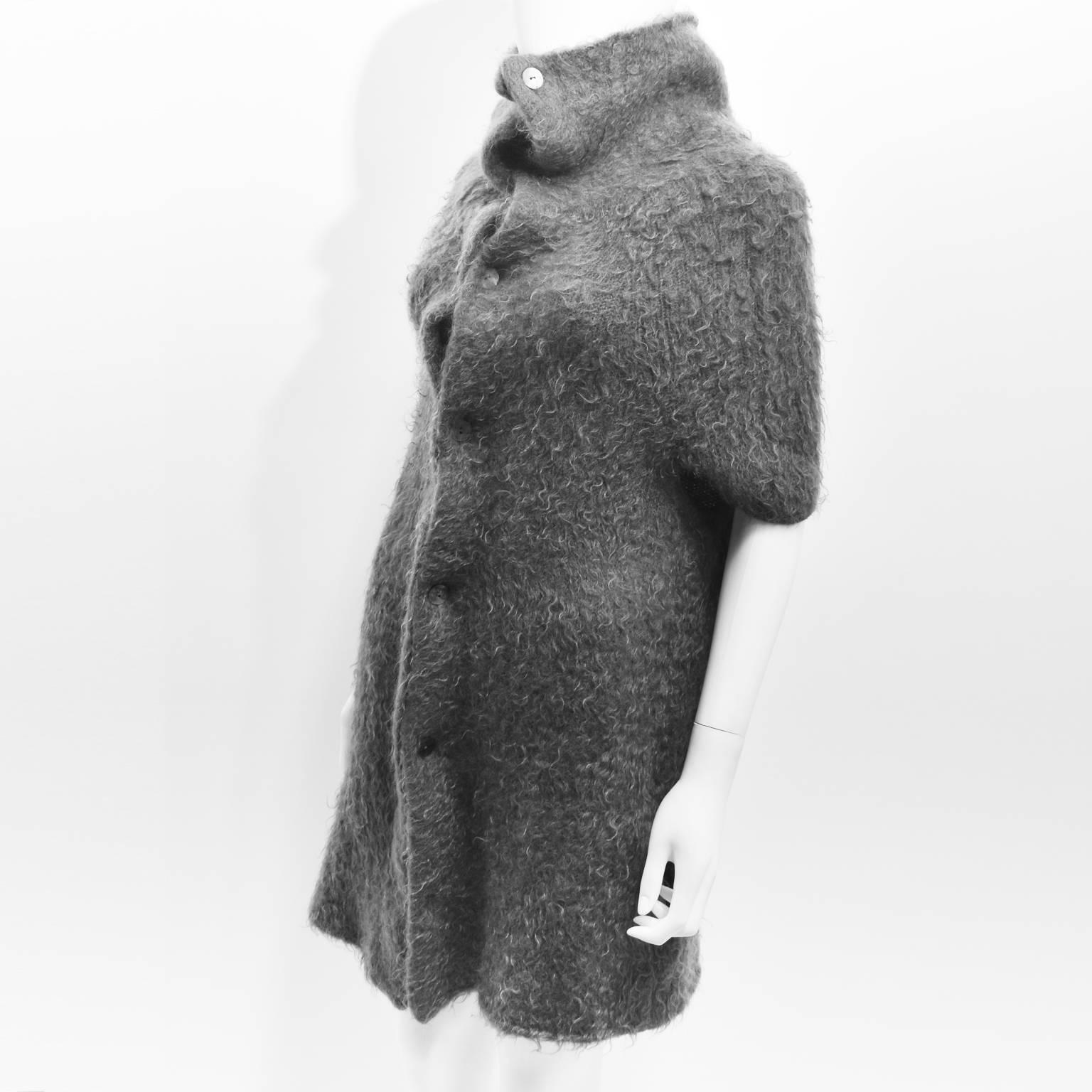 A grey Mohair (80%) knit by Maison Martin Margiela featuring a buttoned front, round short raglan sleeves (seams are concealed), a turtleneck and two side pockets. Size S.