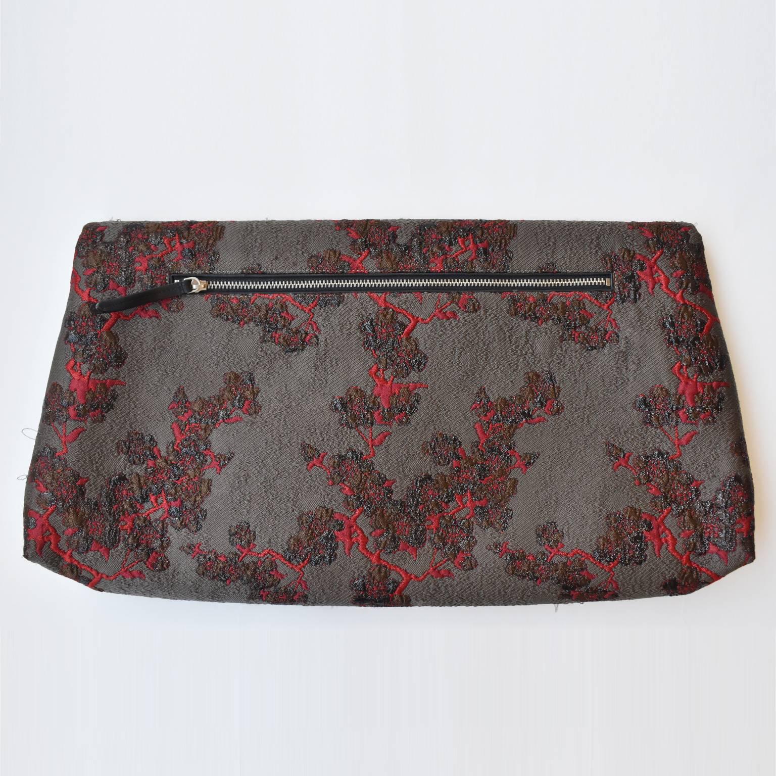 A  grey and burgundy blossom jacquard envelope clutch by Dries Van Noten. It features a leather lining, a back zip pocket, and a magnetic fastening. It comes with dustbag. It has a few pulls (see pictures), otherwise in excellent condition.
