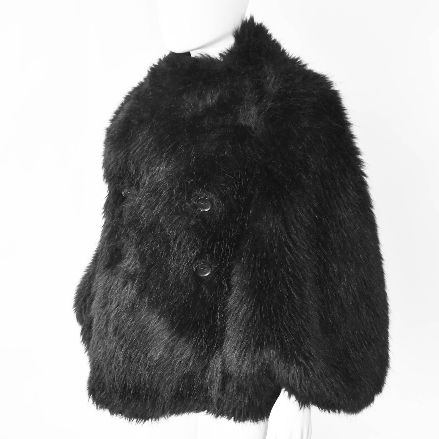 A black faux-fur cape-like double-breasted jacket with faux-leather lining by Junya Watanabe from 2011. It features large buttons, two tabs to inserts arms, two inside pockets and a shorter back hem. In excellent condition. It is an S, but can fit a