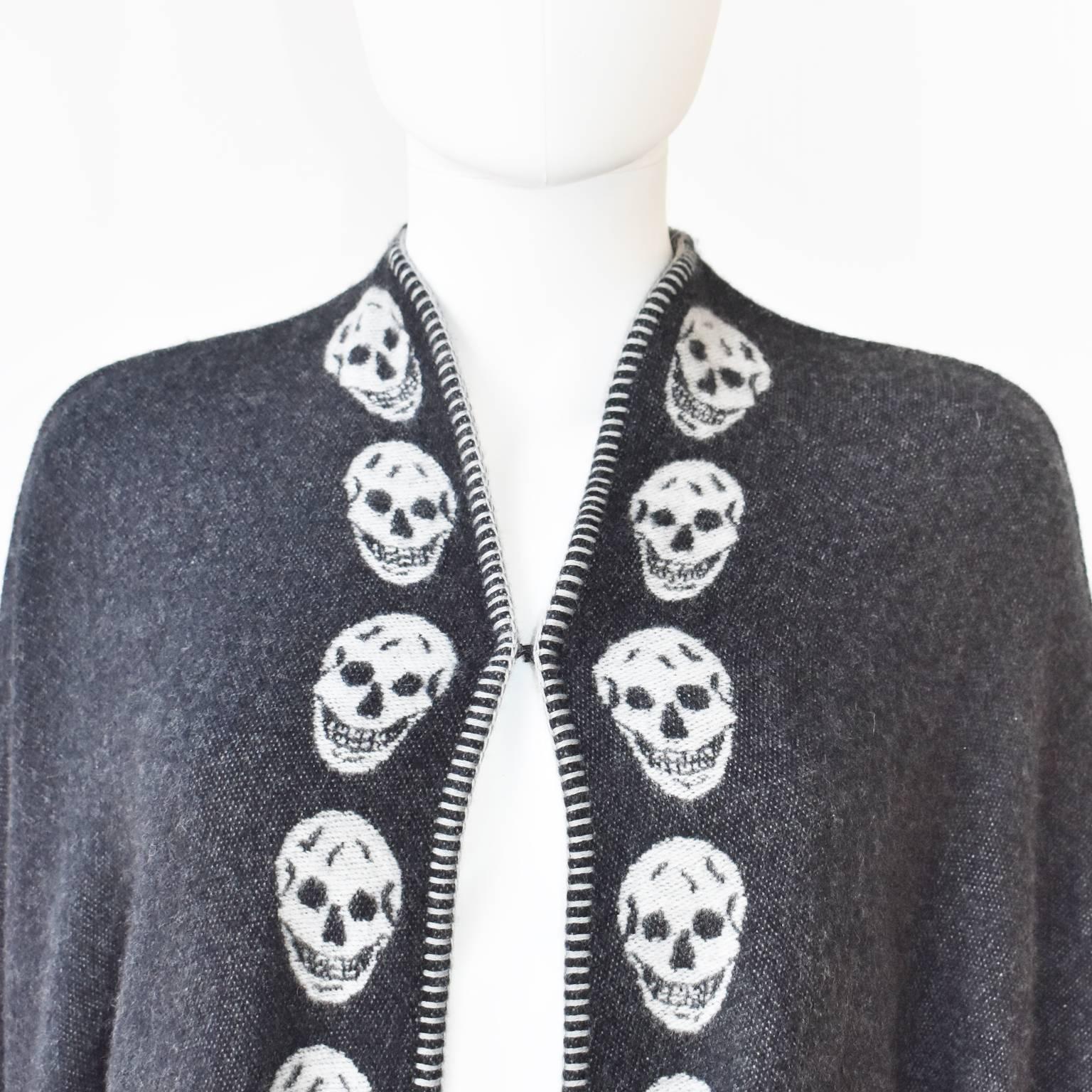 A grey cashmere cape with white skull motifs by Alexander Mcqueen. It features a small hook fastening. It is a sample, it is like new. Free size.