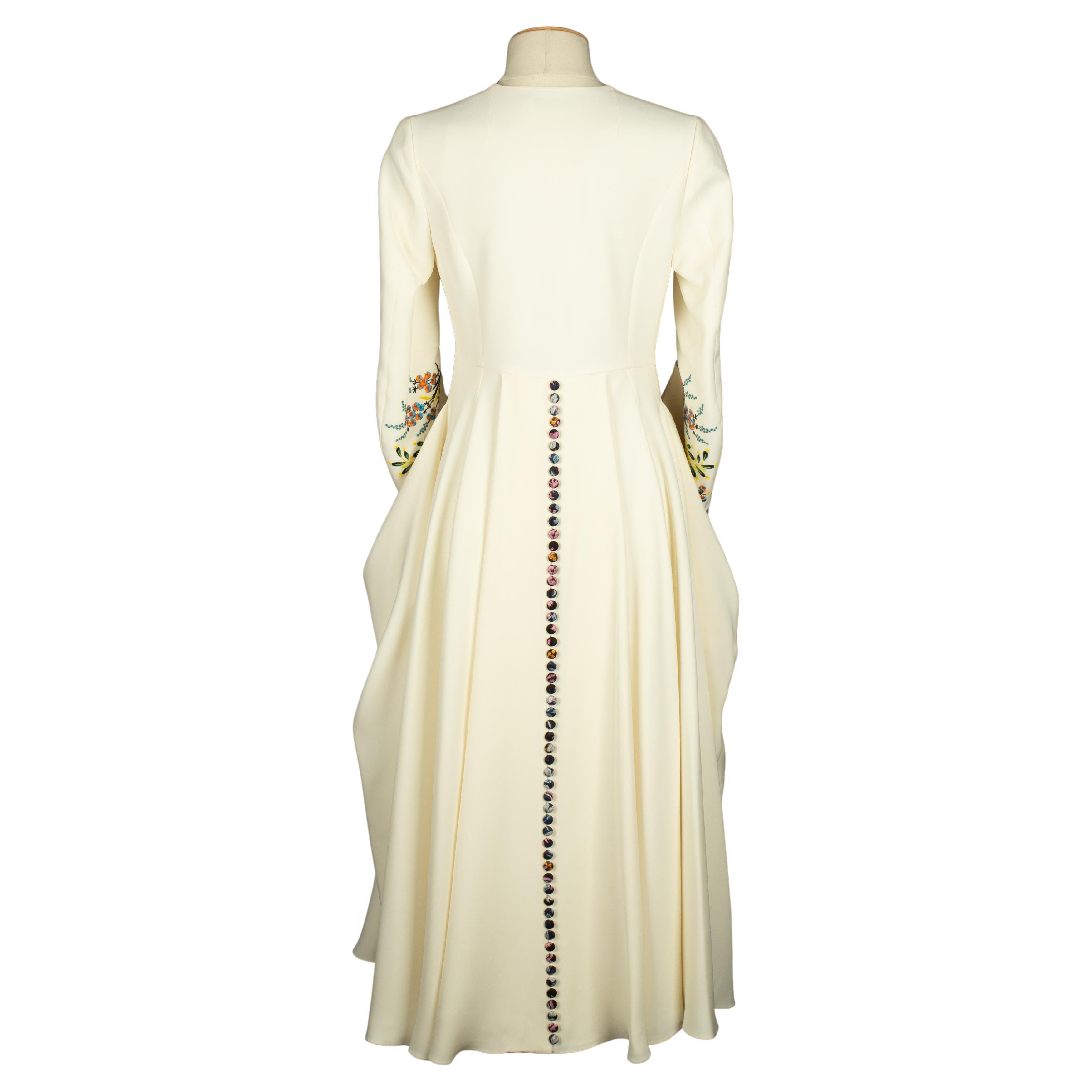 DIOR - (Fabriqué en France) Robe manteau en soie blanc cassé, bas de manches brodés d'un motif de fleurs multicolores. Taille 34FR indiquée. Collection printemps-été 2015 sous la direction artistique de Raf Simons.

Condit :
Très bon