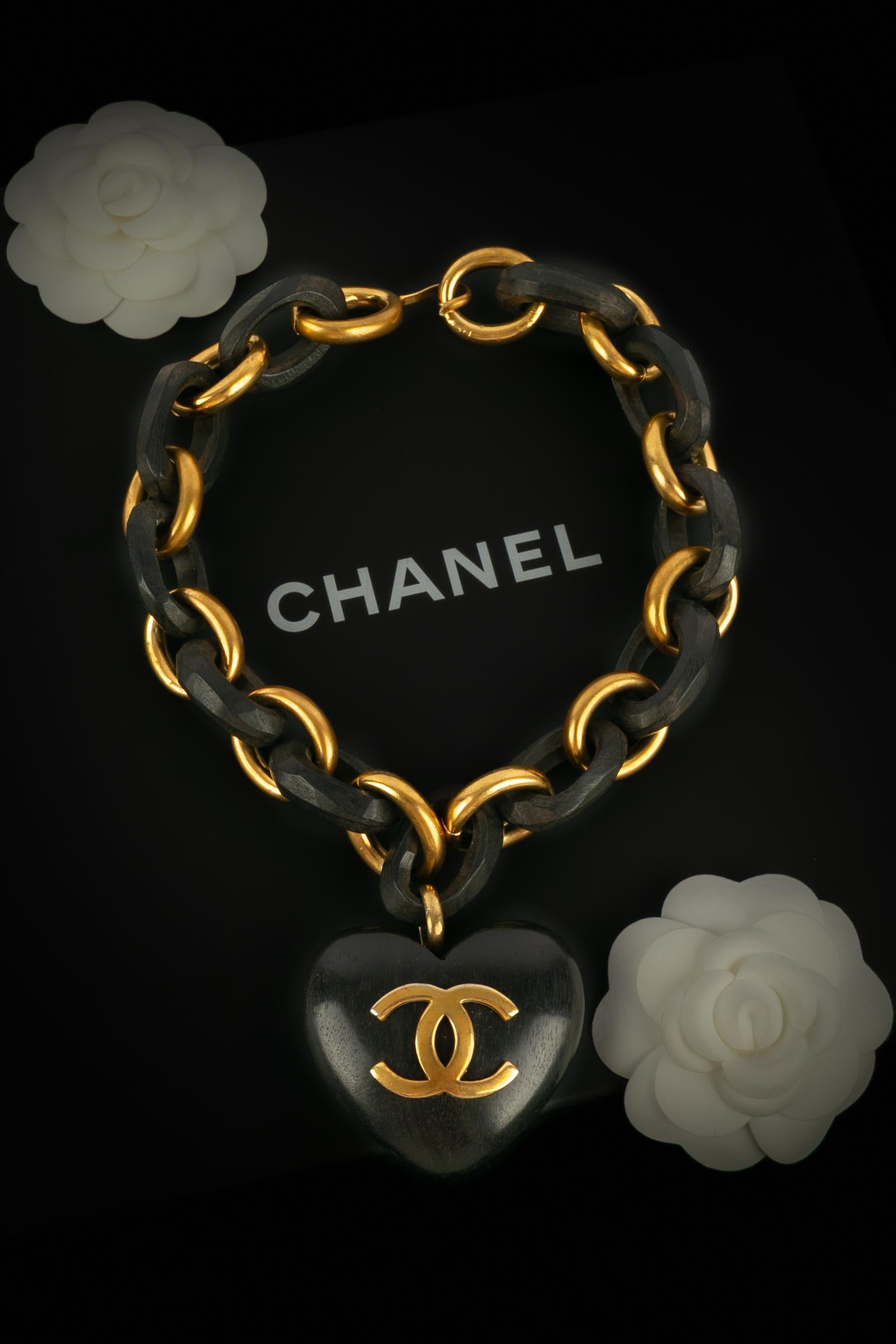 CHANEL - (Fabriqué en France) Collier chaîne iconique composé d'anneaux en métal doré et d'anneaux en bois, avec un pendentif en forme de cœur en bois. Collectional printemps-été 1992 sous la direction artistique de Karl Lagerfeld.

Condit :
Très