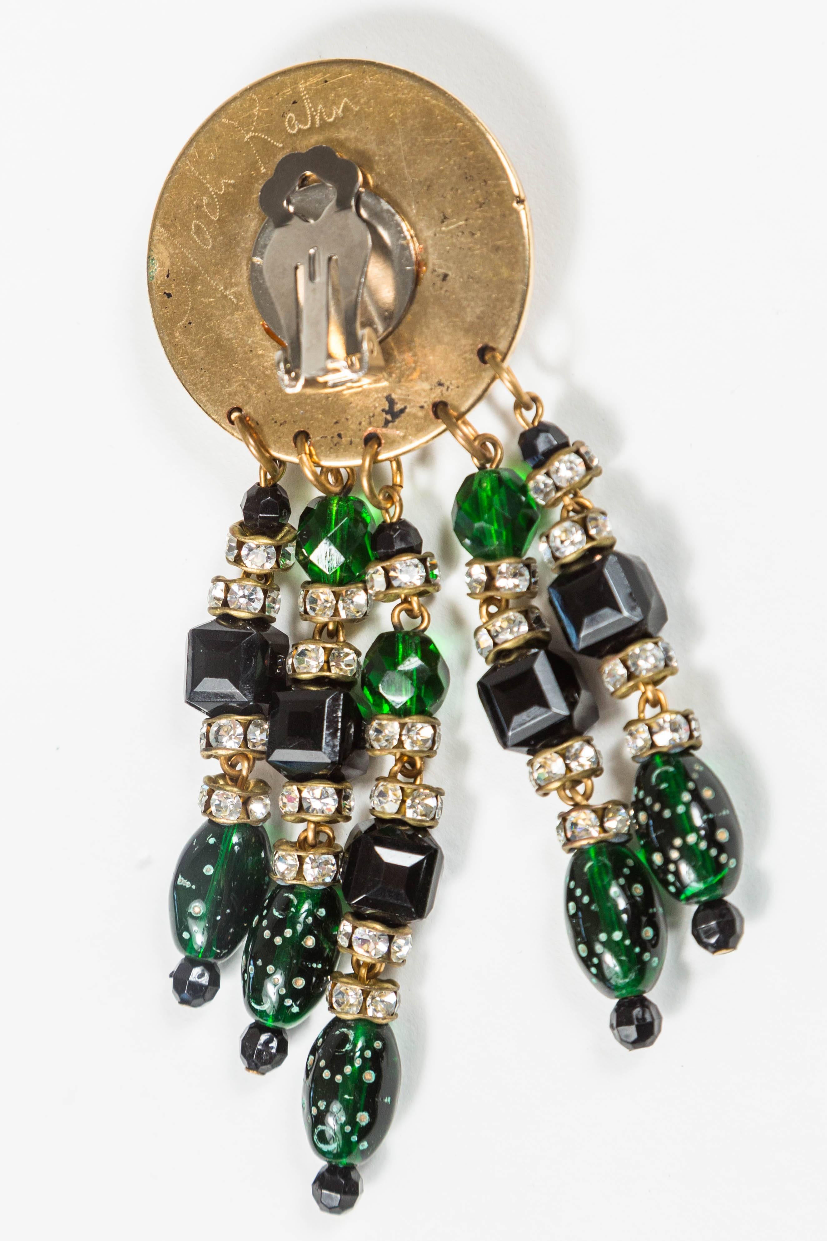 Pair of bewitching costume ear clips by Jodi Kahn. Each with a black center stone surrounded in rhinestones on a gilt pendant, with green and rhinestone beaded drops. Signed Jodi Kahn on the reverse. The ear clip 1 1/4 inches in diameter. 4 inches