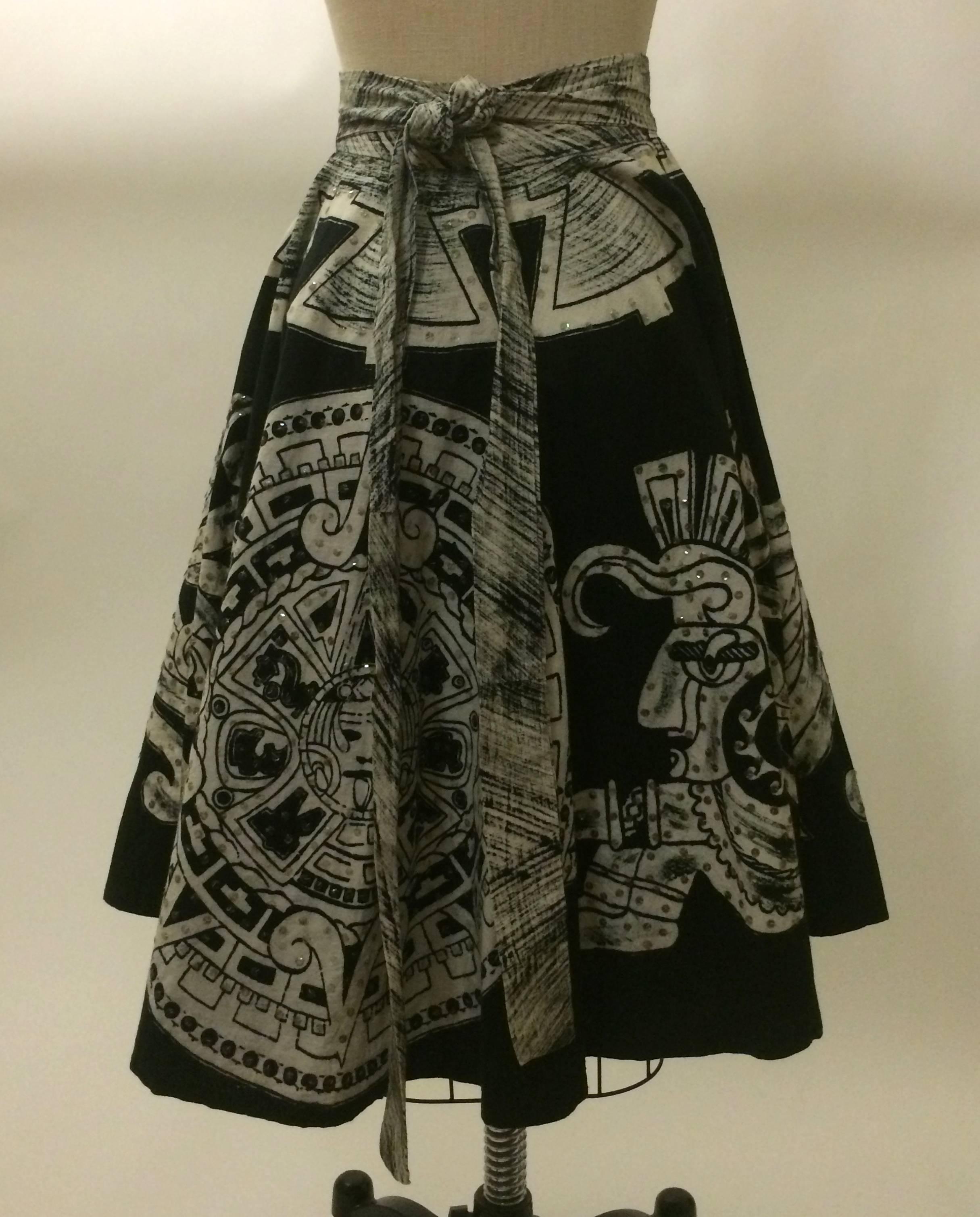 Black full skirt encircled with white Aztec calendar & warriors. Two short straps from the back panel wrap around the waist and fasten with two hook and eye closures, while two longer straps attached to the front panel tie over them to conceal the