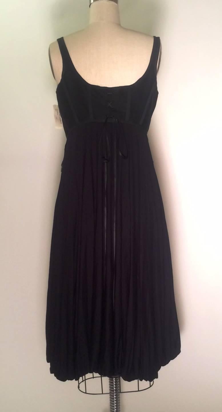 Alexander McQueen 2004 black sleeveless dress with corset detailing at top and bubble hem. Midi length. Four small buttons at chest and hidden snap. Antiqued d-ring hardware hanging at sides and long ribbons lace up the back (you can tie these at