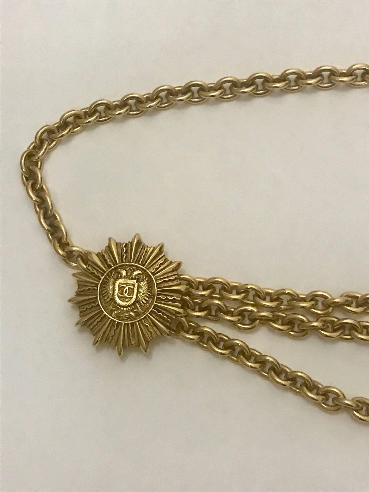 Chanel vintage 1980's gold tone chain belt featuring sunburst medallions with eagles and logo shields at center. Triple chain at front. Hanging CC logo.

Closes with hook at back of medallion.

Stamped '(copyright) Chanel (registered), CC, Made