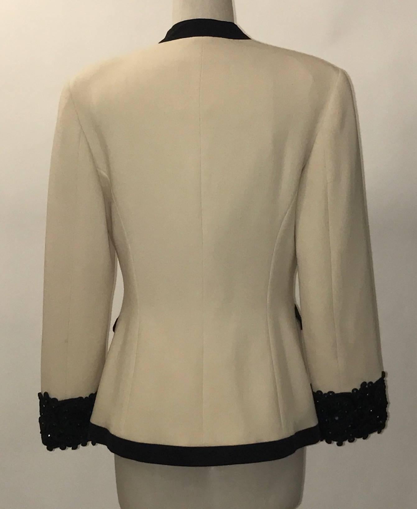 Cream wool crepe Genny blazer with three beaded snap closures at front and bead and sequin embellished cuffs. Black trim at pockets and edges. Fully lined, shoulder pads of mid-thickness.

100% wool.
Trimmed in 68% cotton, 32% viscose. 
Fully