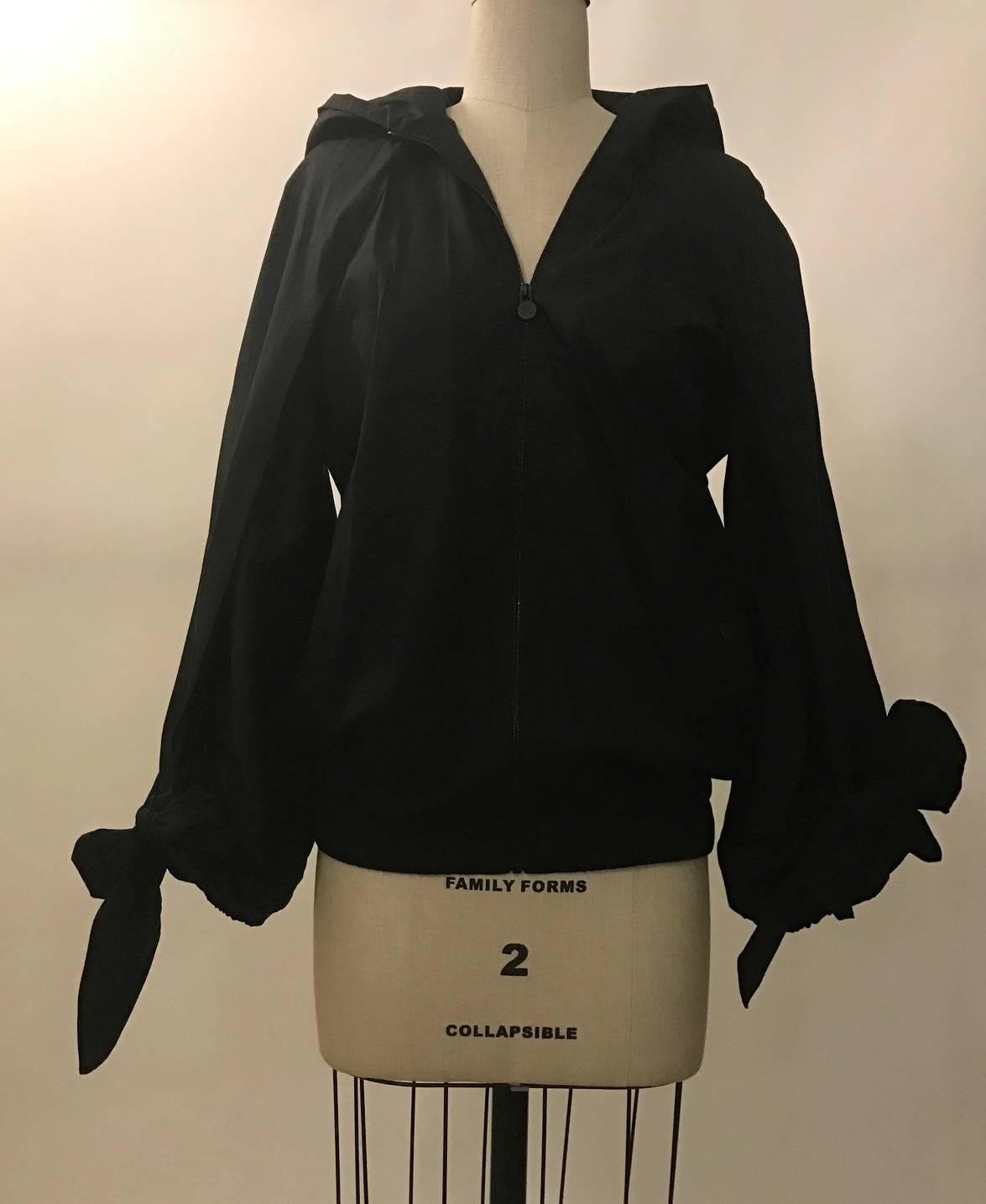Chanel black windbreaker with slit balloon sleeves finished with ties at bottom and super long detachable scarf that can be tied in a bow, wrapped, or left hanging. Hooded, zip front and snap pockets feature CC logo.

Cruise/resort 2015 runway look