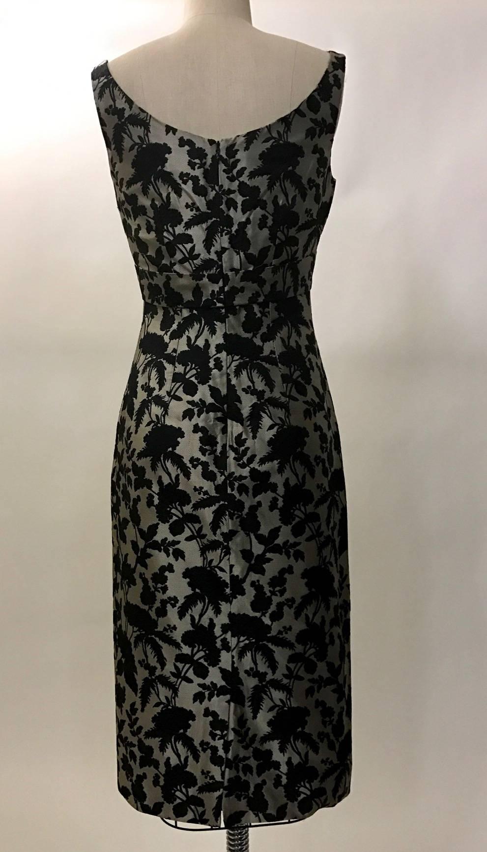 Alexander McQueen 2006 grey and black floral brocade sleeveless fitted dress with pleated detailing at chest. Subtle strap detail comes from sides and crosses at chest to meet at back zip. Back zip and hook and eye.

100% silk.
Fully lined in 85%