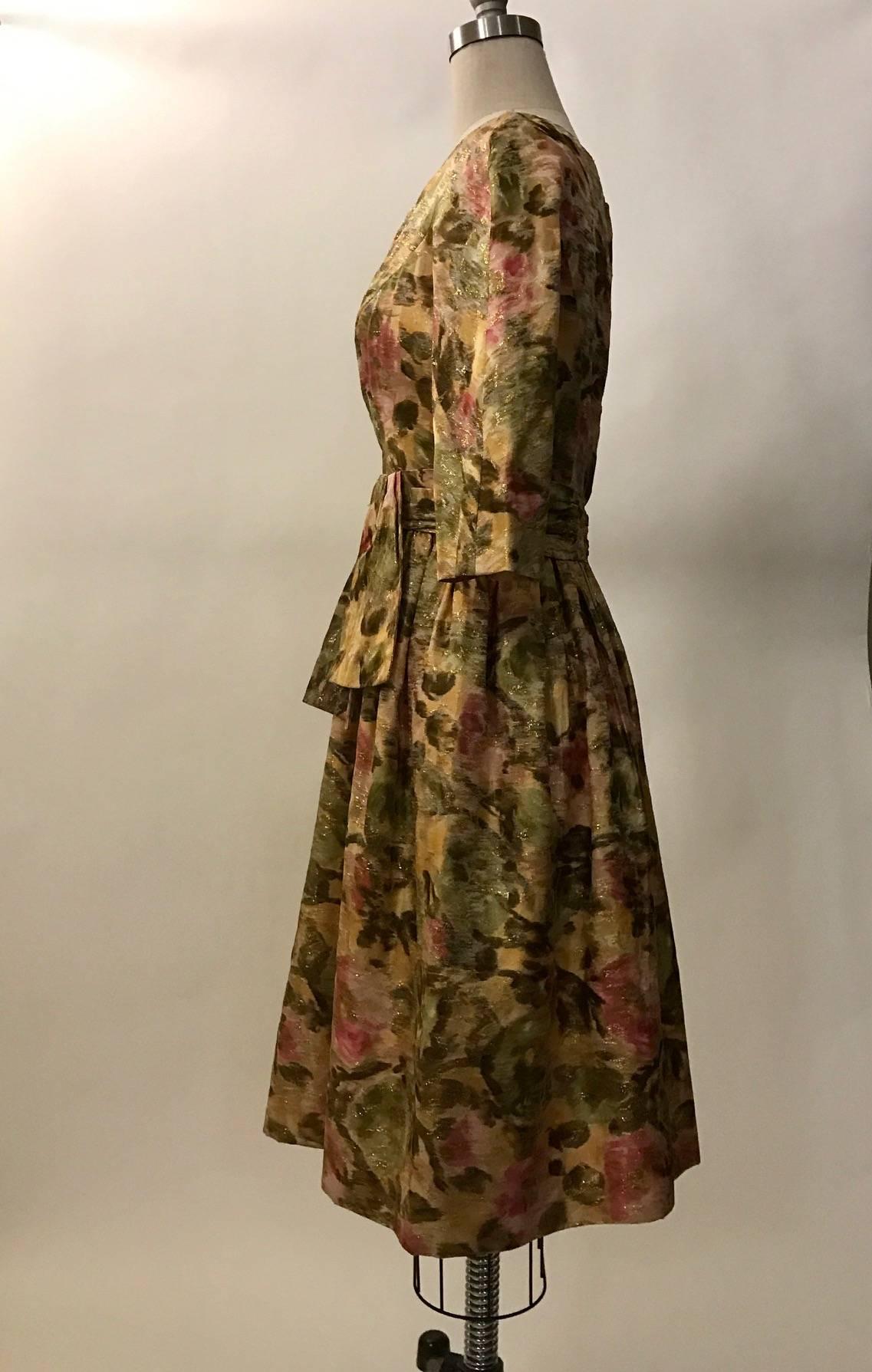Wilson Folmar for Edward Abbott late 1950's metallic cream, pink, green, and gold floral print dress. Boat neck and bow detail at waist. Mid length sleeves. Back zip with hook and eyes at top zip and waist detail.

Perfect for a tea or garden