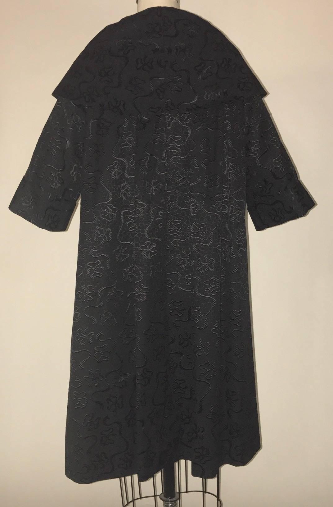 I Magnin & Co late 1950s black jacquard bow print swing coat. Three buttons at front. Mid length sleeve and large shawl collar. Pockets at side seams.

Content unknown.
Fully lined.

No size label, see measurements. Shoulders best fit an XS, but may